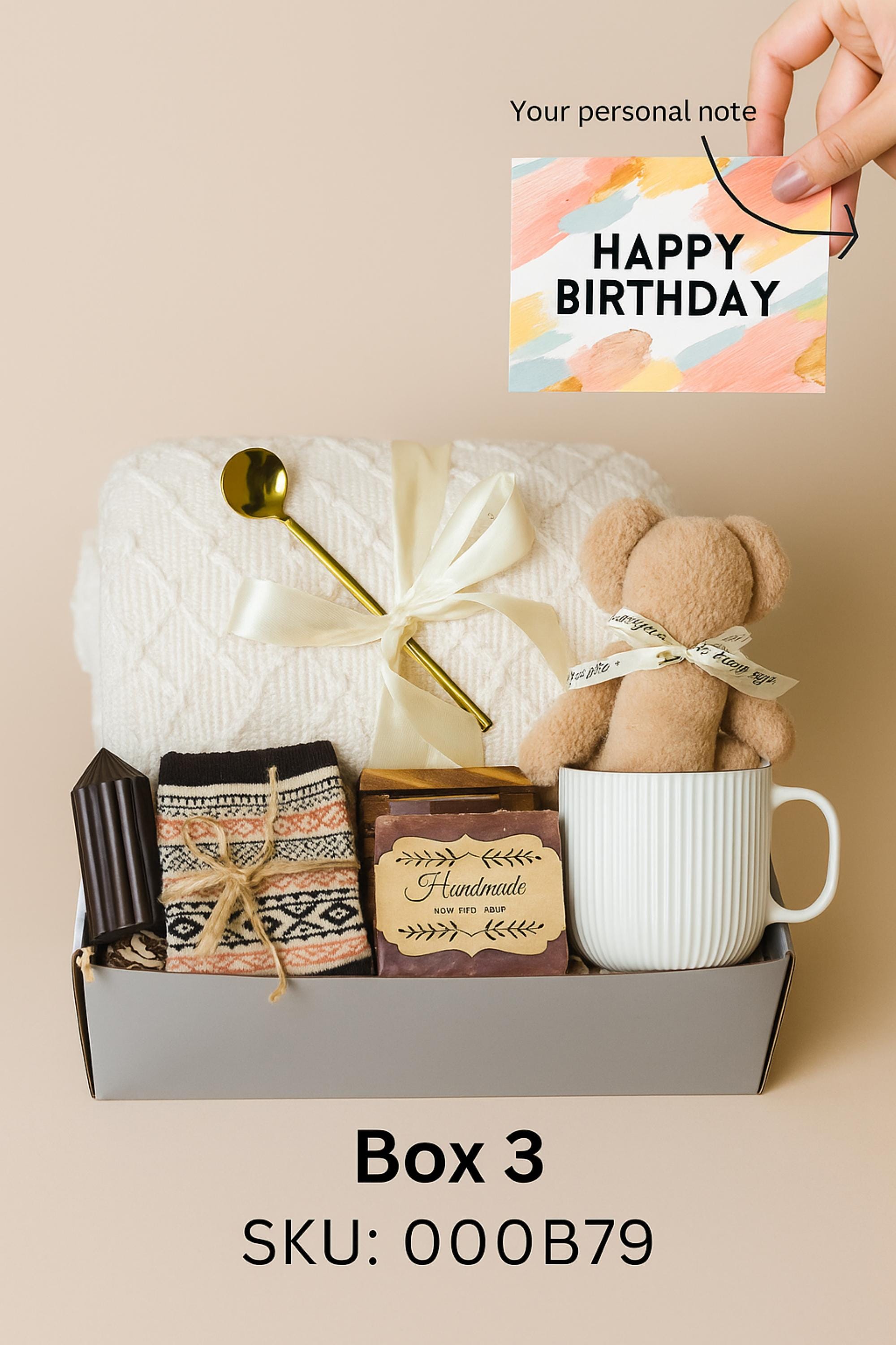 Winter self-care gift box featuring a cozy white blanket with ribbon, a teddy-bear-shaped washcloth, handmade pink and blue soap on a wooden tray, and a soft crocheted bear sitting in a white mug. Displayed on a rustic wood surface with snowy accents, this cozy winter spa set makes a thoughtful holiday comfort gift, pamper box, relaxation present, or get-well care package for women.