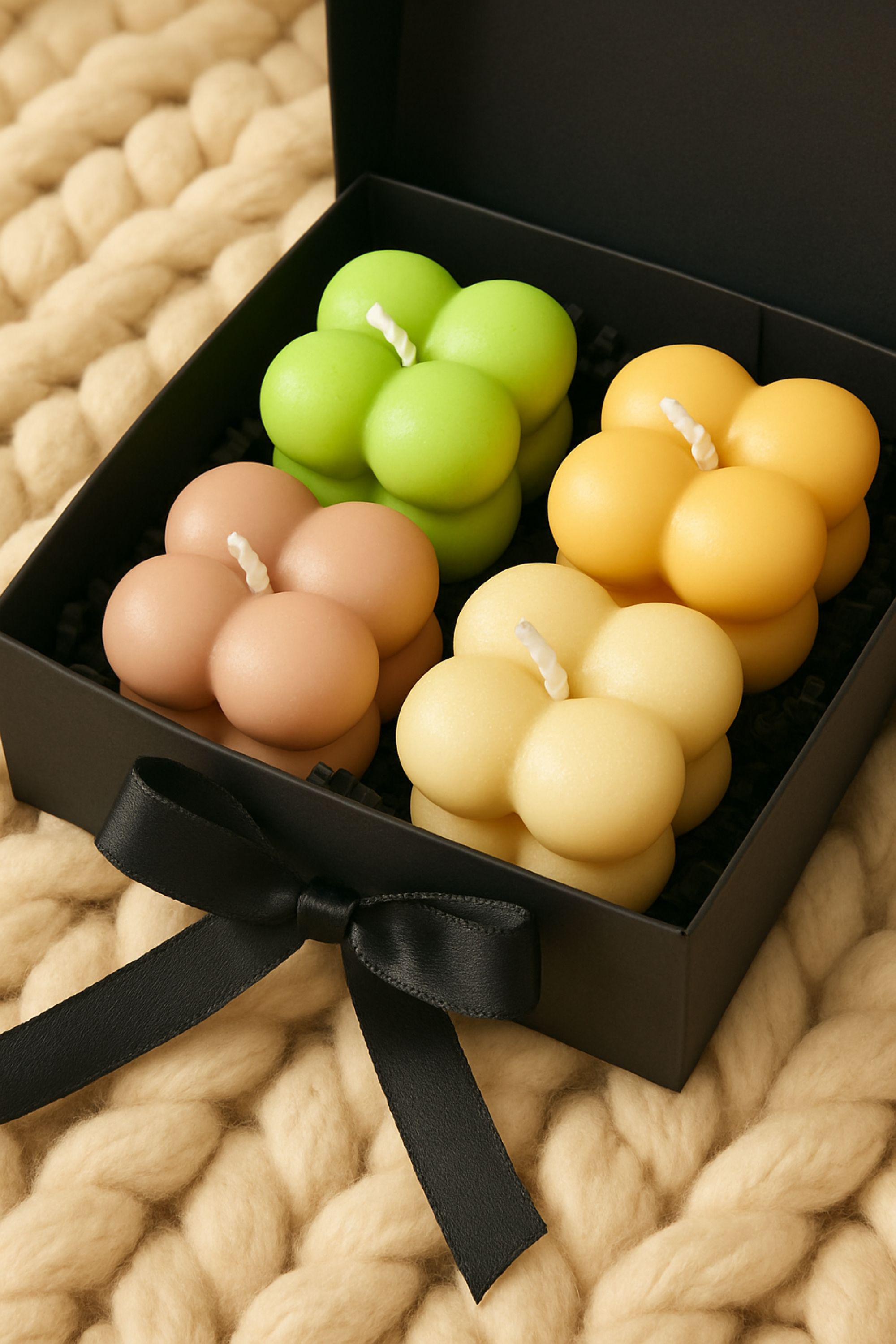 Open black Christmas gift box showing pastel bubble candles inside, styled on a wooden surface with holiday decorations. Bubble candle gift set and cozy holiday self-care present.