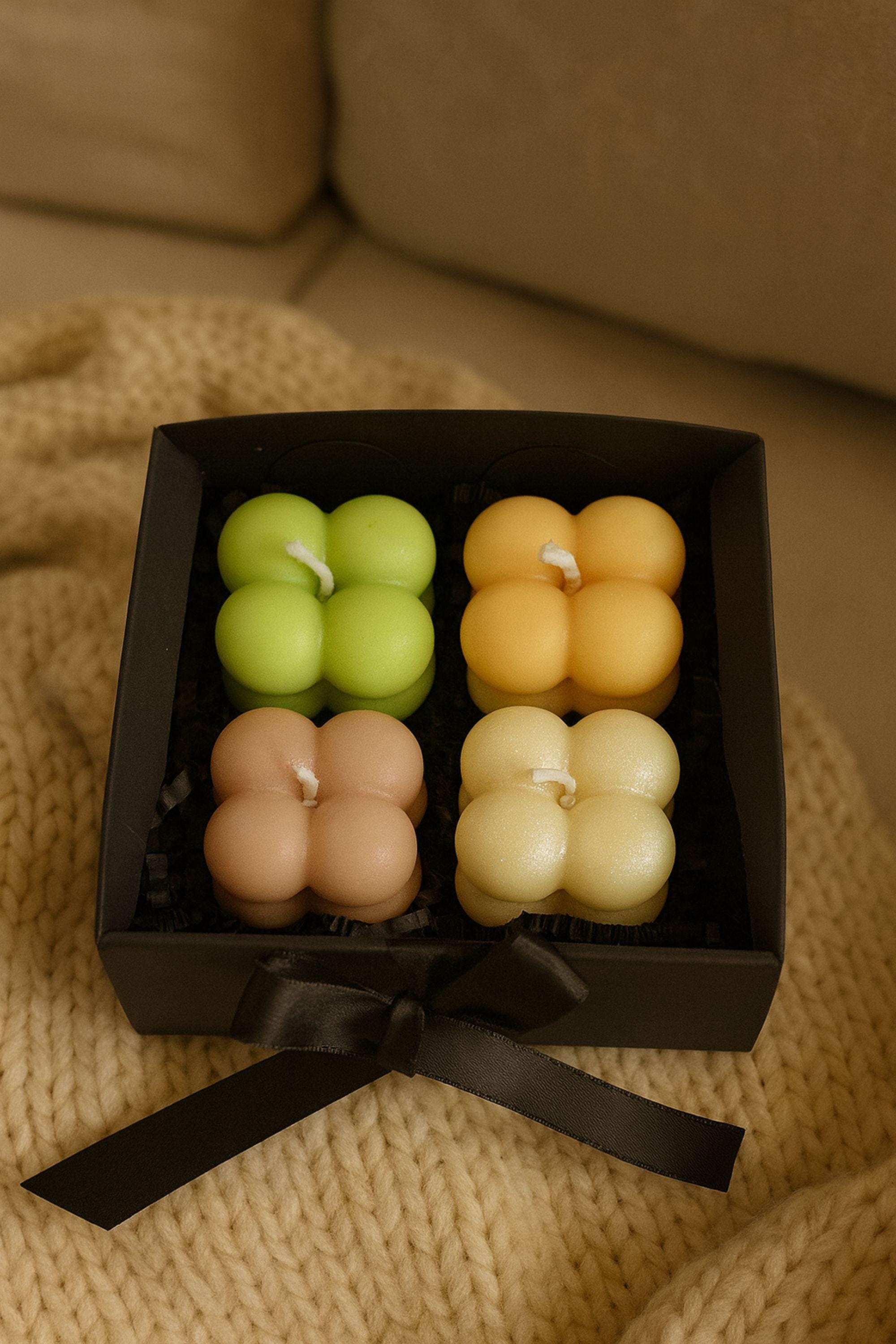 Overhead view of four pastel bubble candles arranged in a black gift box with black crinkle paper. Minimalist Christmas candle gift box, hygge decor and stocking stuffer for women.
