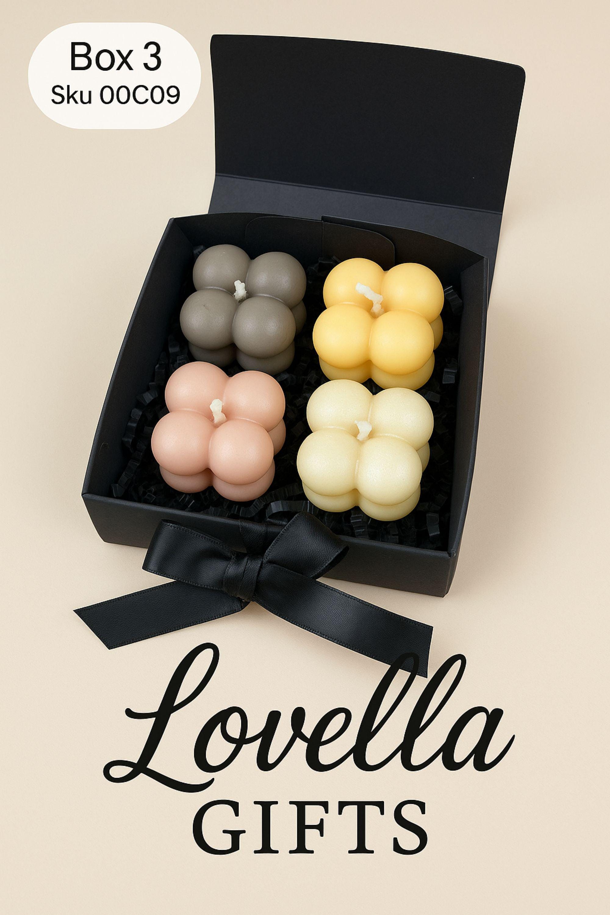 Christmas bubble candle gift box with four pastel mini bubble candles in a black box with ribbon, styled with festive greenery and ornaments. Cozy holiday spa gift set and small Christmas present for her.