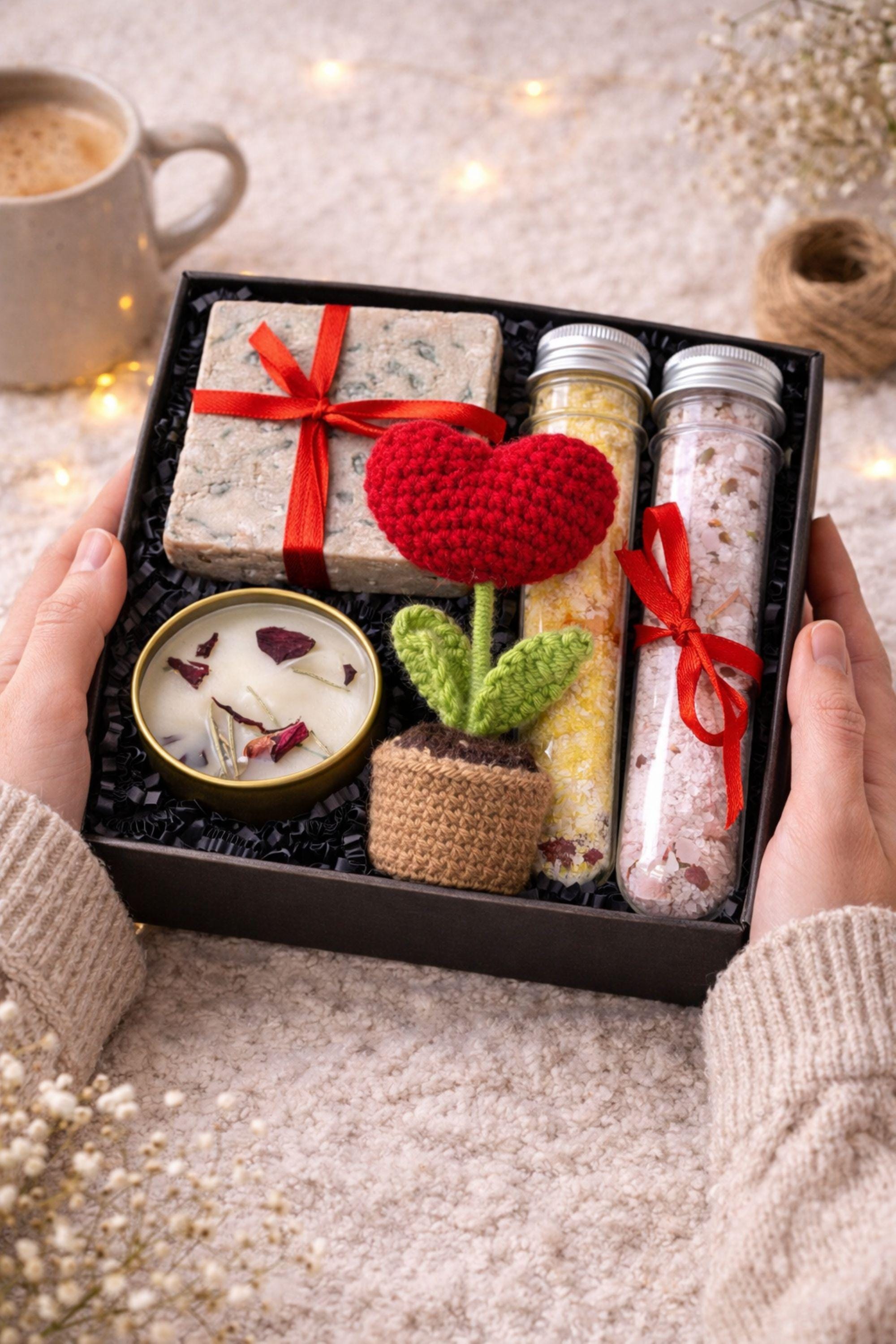 Handmade crochet flower gift box with crochet flower in a pot, handmade soap, botanical candle in a tin, and two bath salt tubes arranged in a black gift box. Thoughtful comfort gift designed to show care and appreciation. Perfect thinking of you gift, friendship gift, or unique handmade present for her, beautifully packaged and ready to give.
