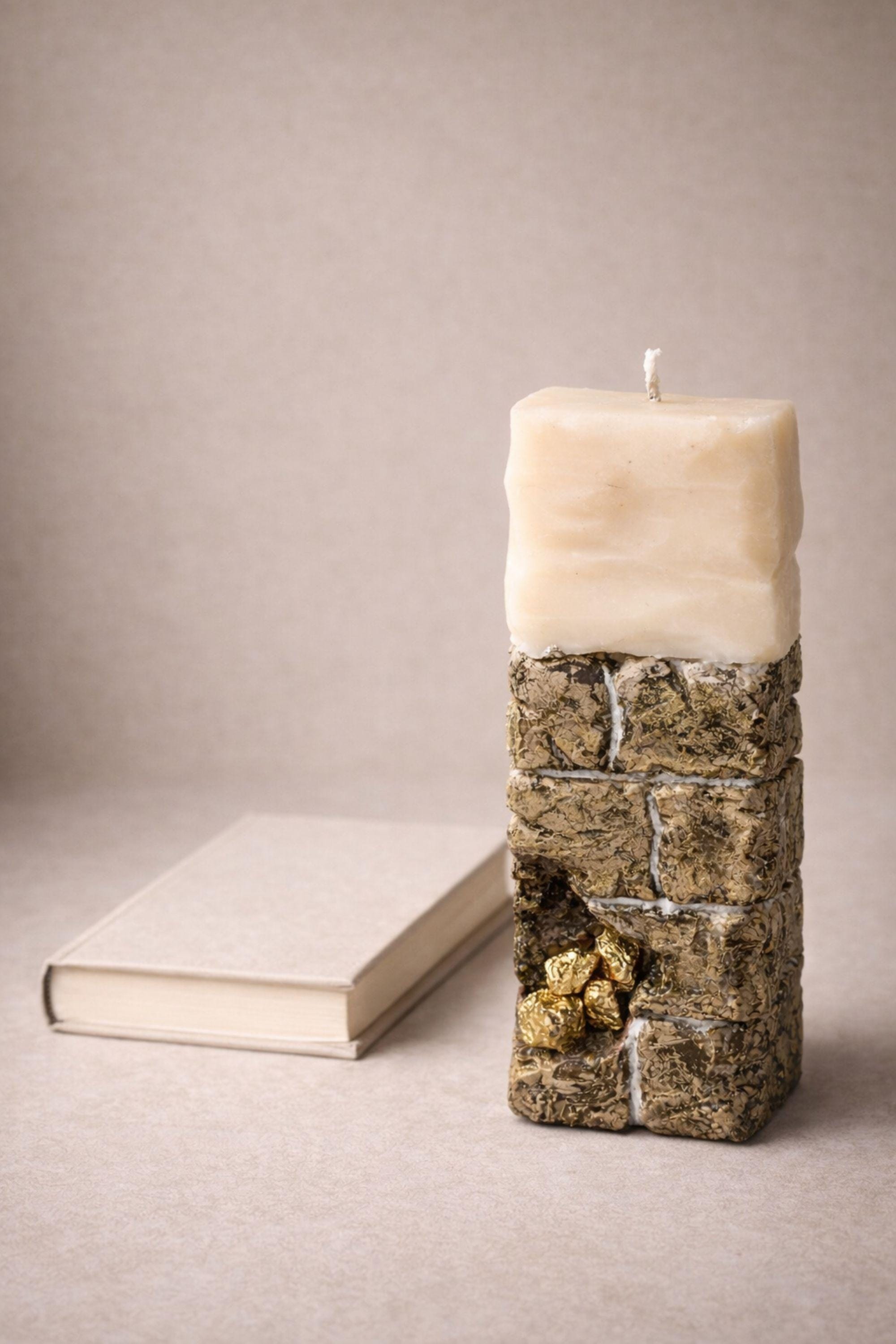 Sculptural ritual candle handmade from wax with textured stone-inspired surface and metallic gold detailing, designed as a modern altar decor object. Minimalist sculptural candle that can be displayed as art or burned intentionally. Artisan wax sculpture candle for ritual space, meditation altar, or modern interior decor. Unique handcrafted statement candle with raw texture and architectural form, photographed on neutral background.