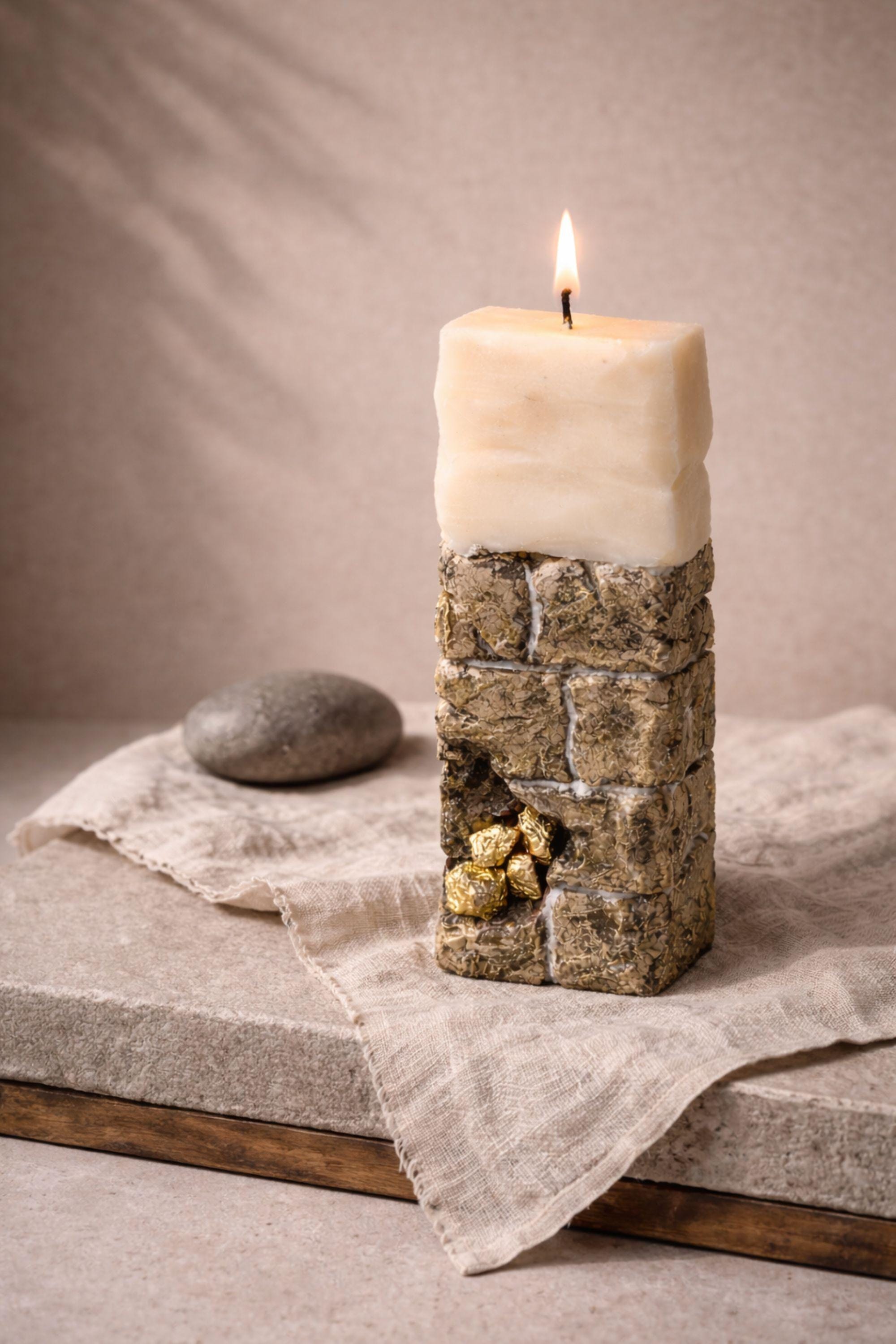 Sculptural ritual candle handmade from wax with textured stone-inspired surface and metallic gold detailing, designed as a modern altar decor object. Minimalist sculptural candle that can be displayed as art or burned intentionally. Artisan wax sculpture candle for ritual space, meditation altar, or modern interior decor. Unique handcrafted statement candle with raw texture and architectural form, photographed on neutral background.