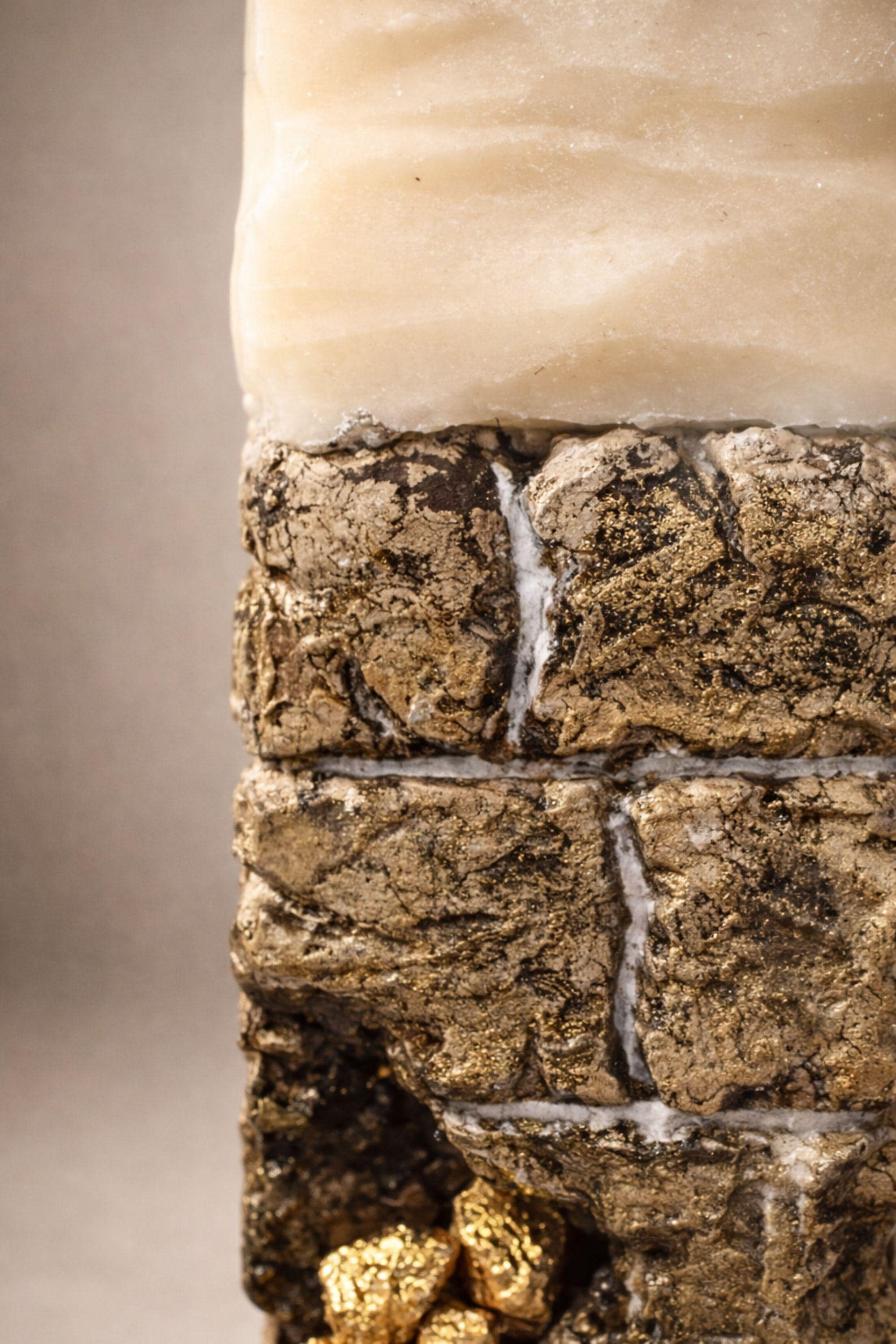 Sculptural ritual candle handmade from wax with textured stone-inspired surface and metallic gold detailing, designed as a modern altar decor object. Minimalist sculptural candle that can be displayed as art or burned intentionally. Artisan wax sculpture candle for ritual space, meditation altar, or modern interior decor. Unique handcrafted statement candle with raw texture and architectural form, photographed on neutral background.