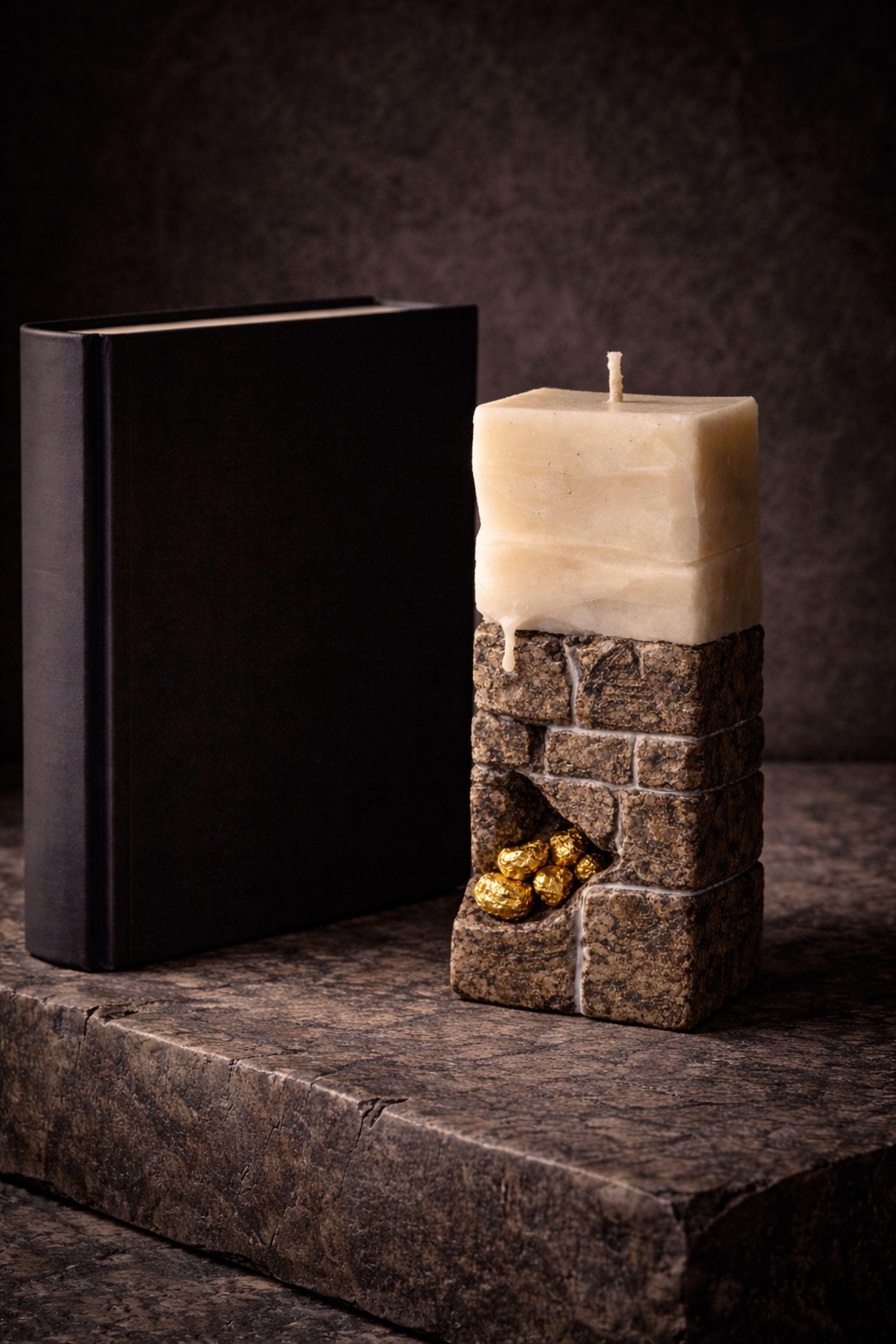Handmade sculptural candle decor with stone texture beside a black book, adding elegance to modern interiors.