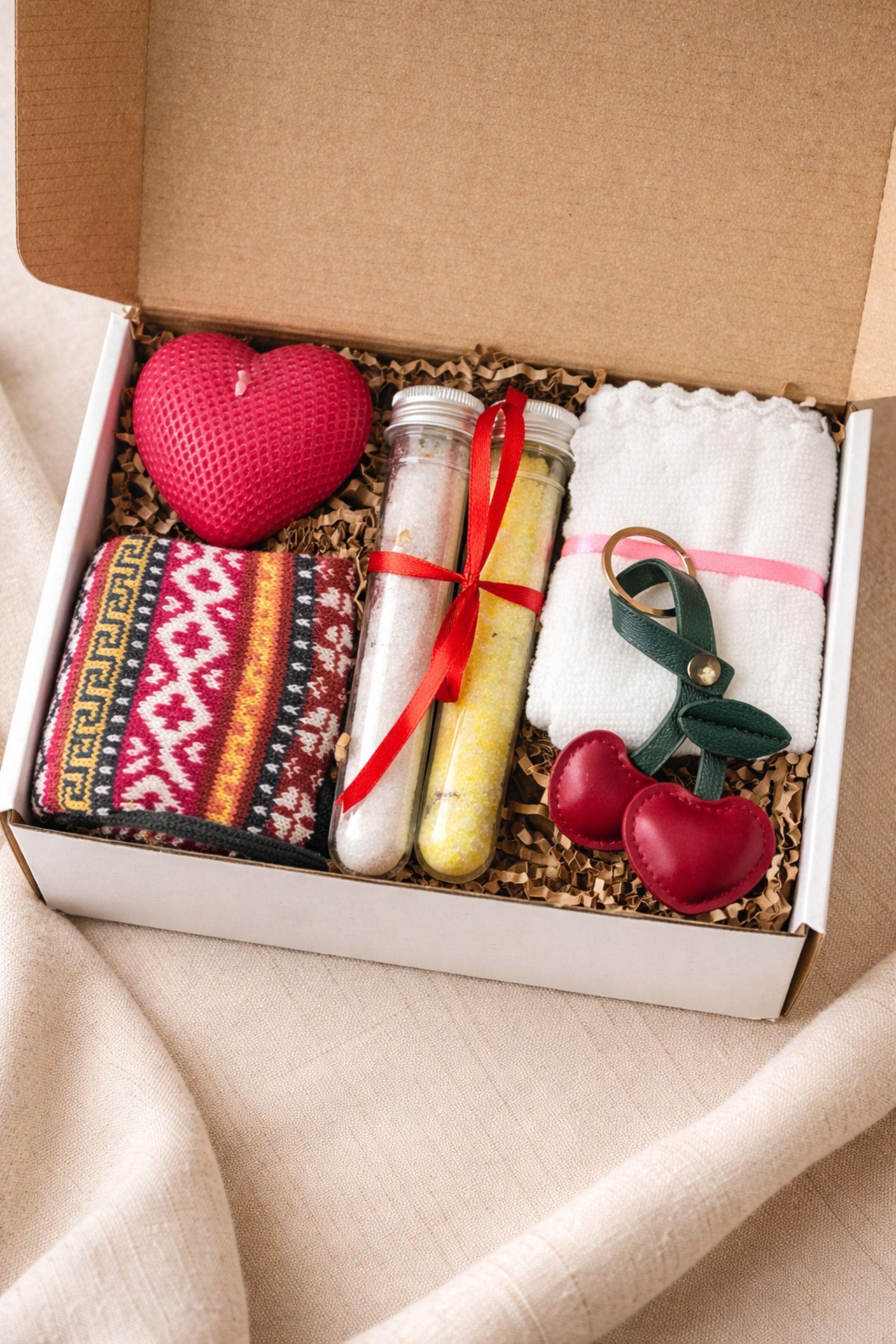 Thinking of you gift box with handmade heart candle, cozy knitted socks, bath salt tubes tied with red ribbon, soft cotton washcloth, and leather heart keychain arranged inside a kraft gift box. Small meaningful comfort gift designed as a care package for her, perfect for sending love, warmth, and support during long distance moments, stressful times, or just because. Handmade cozy gift set ready to give.