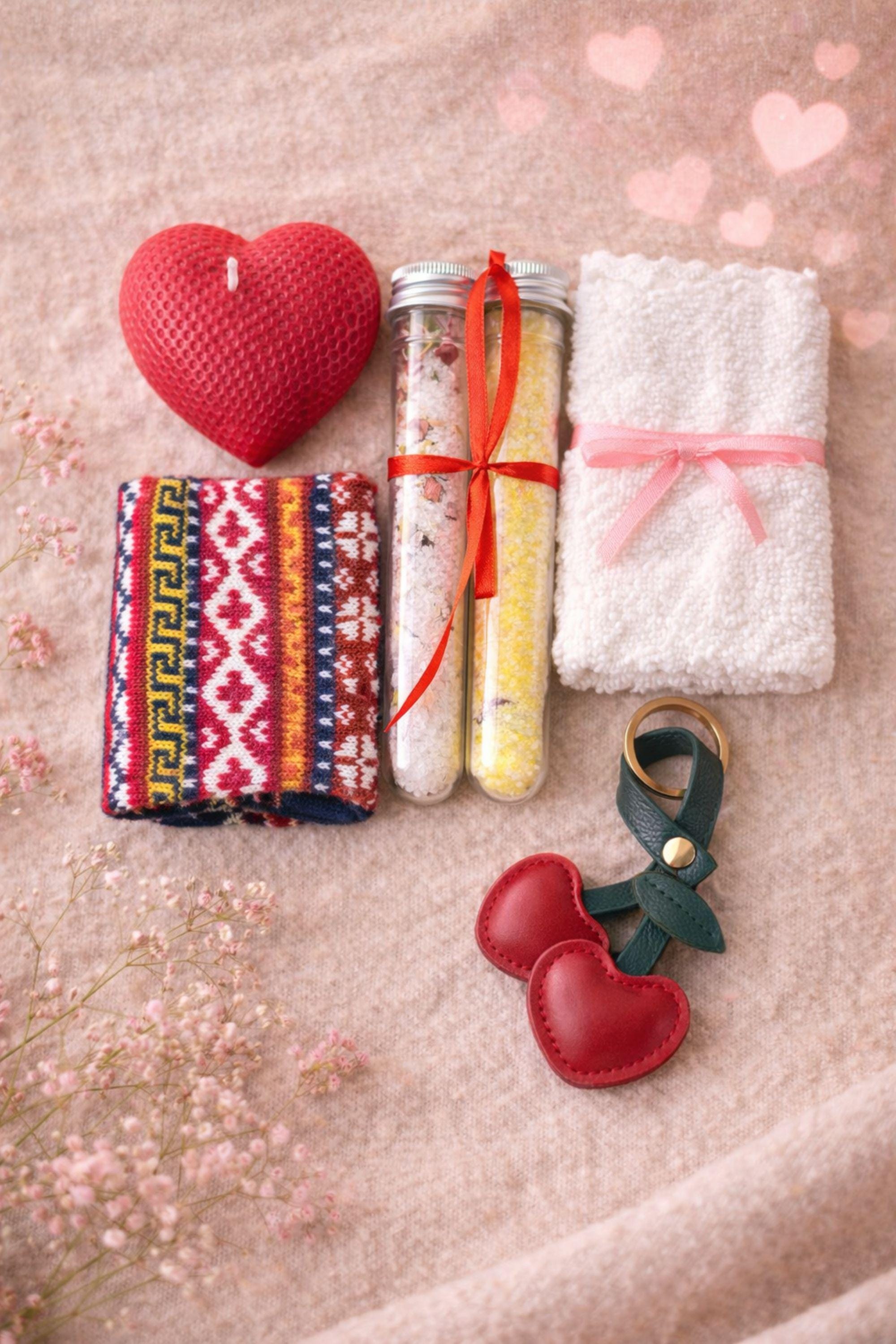 Flat lay of Valentine gift box contents showing handmade heart candle, cozy knit socks, two bath salt tubes, cotton washcloth, and leather heart keychain arranged neatly on neutral fabric. Handmade Valentine care package for her designed as a cozy, romantic gift box, perfect for Valentine’s Day, anniversaries, or sending love and comfort from afar.