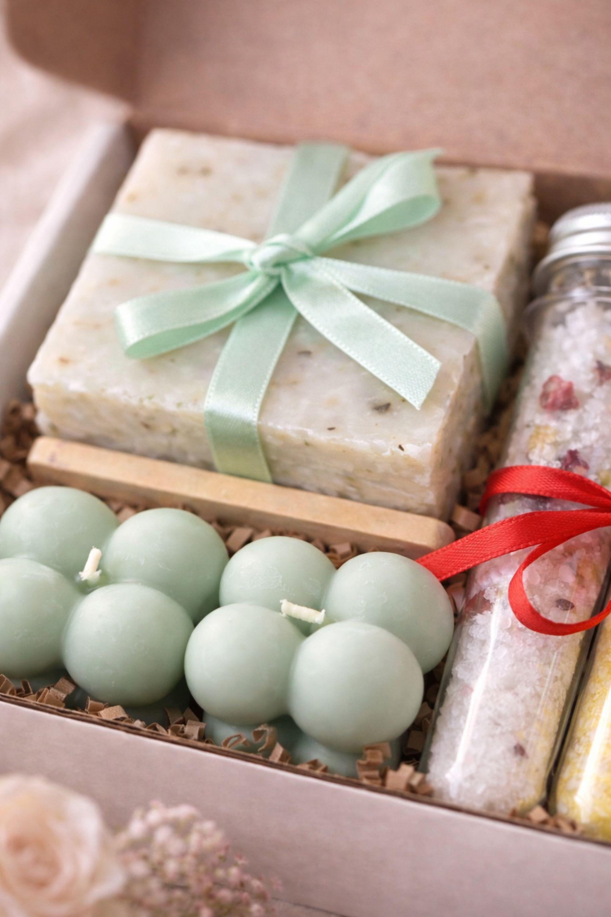 Close-up of handmade sage bubble candles and natural soap with ribbon inside a Valentine gift box, highlighting soft textures and calming colors. Gentle Valentine care package created as a comforting handmade gift for her, ideal for sending calm, care, and warmth through a thoughtful Valentine present focused on relaxation and simplicity.