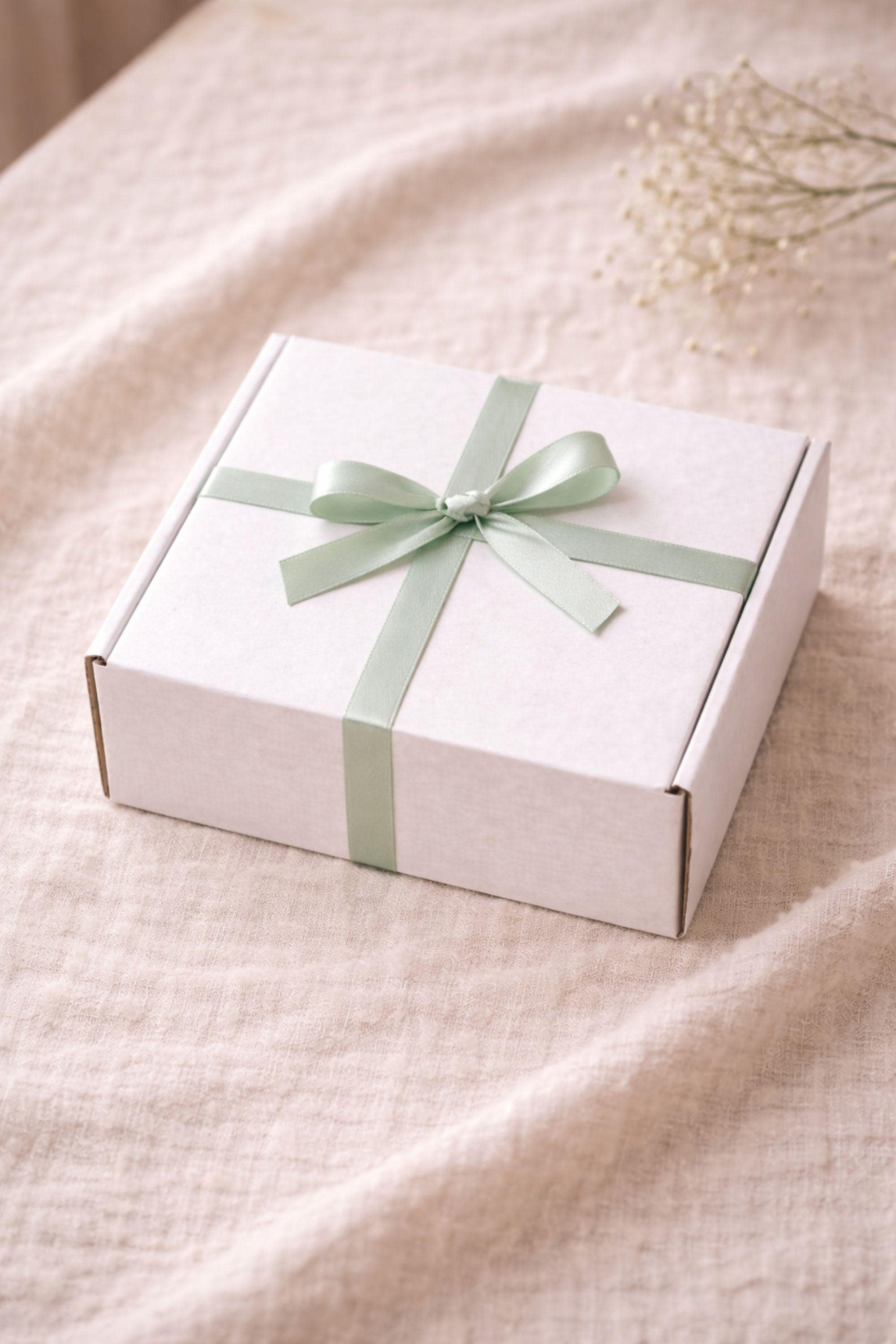 Closed minimalist gift box wrapped with a simple ribbon and placed on a neutral linen background. Handmade candle and soap gift set prepared to enjoy at home or give as a simple, cozy present, designed for calm interiors, everyday use, and minimalist lifestyle gifting without seasonal or emotional themes.
