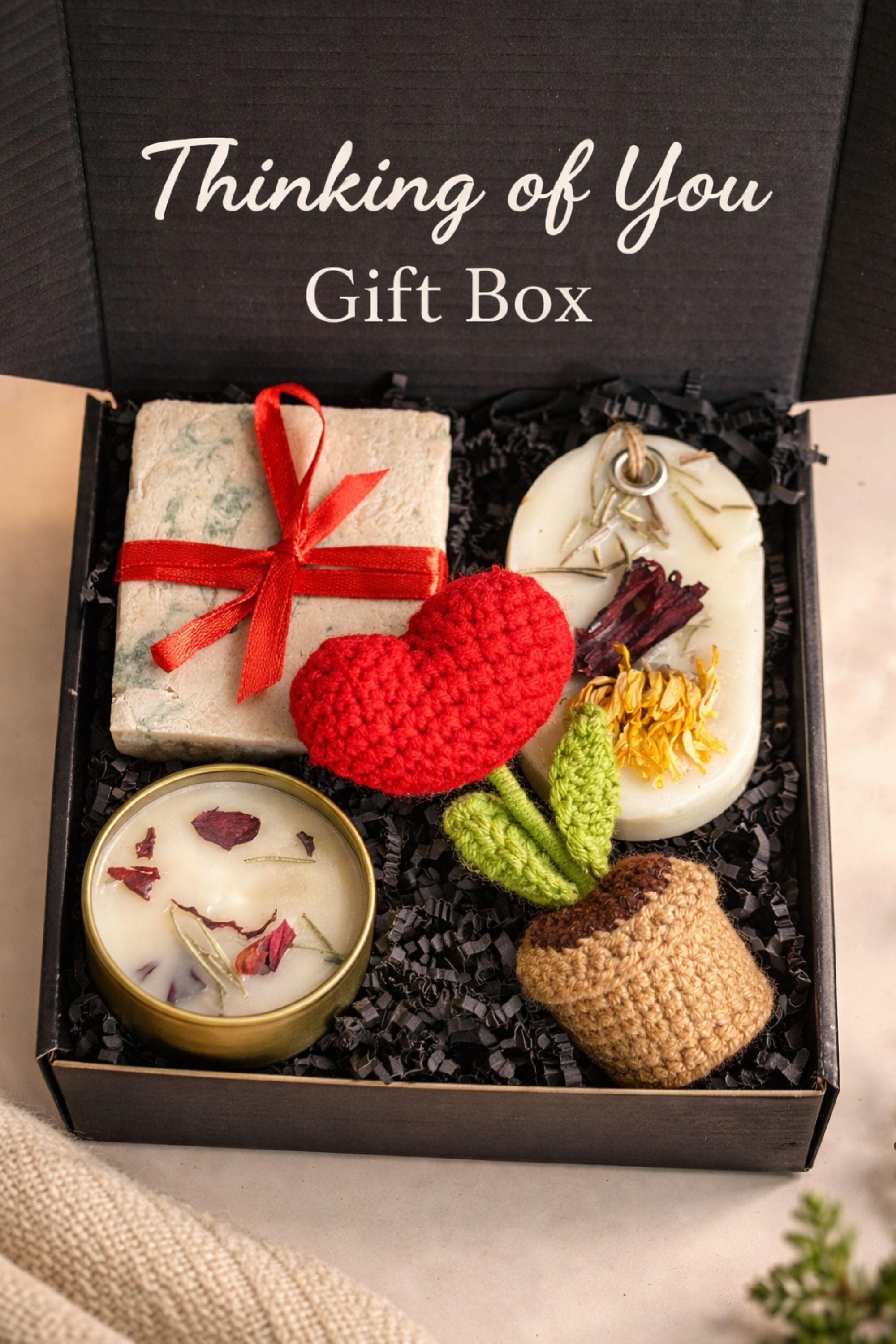 Thinking of you gift box with handmade soap tied with red ribbon, botanical candle in metal tin, wax sachet with dried flowers and crochet flower arranged inside a black gift box. Cozy comfort handmade gift for her, just because care package, small meaningful present for long distance support, encouragement, sympathy or thoughtful gesture. Gift ready handmade box designed to show care, warmth and attention.