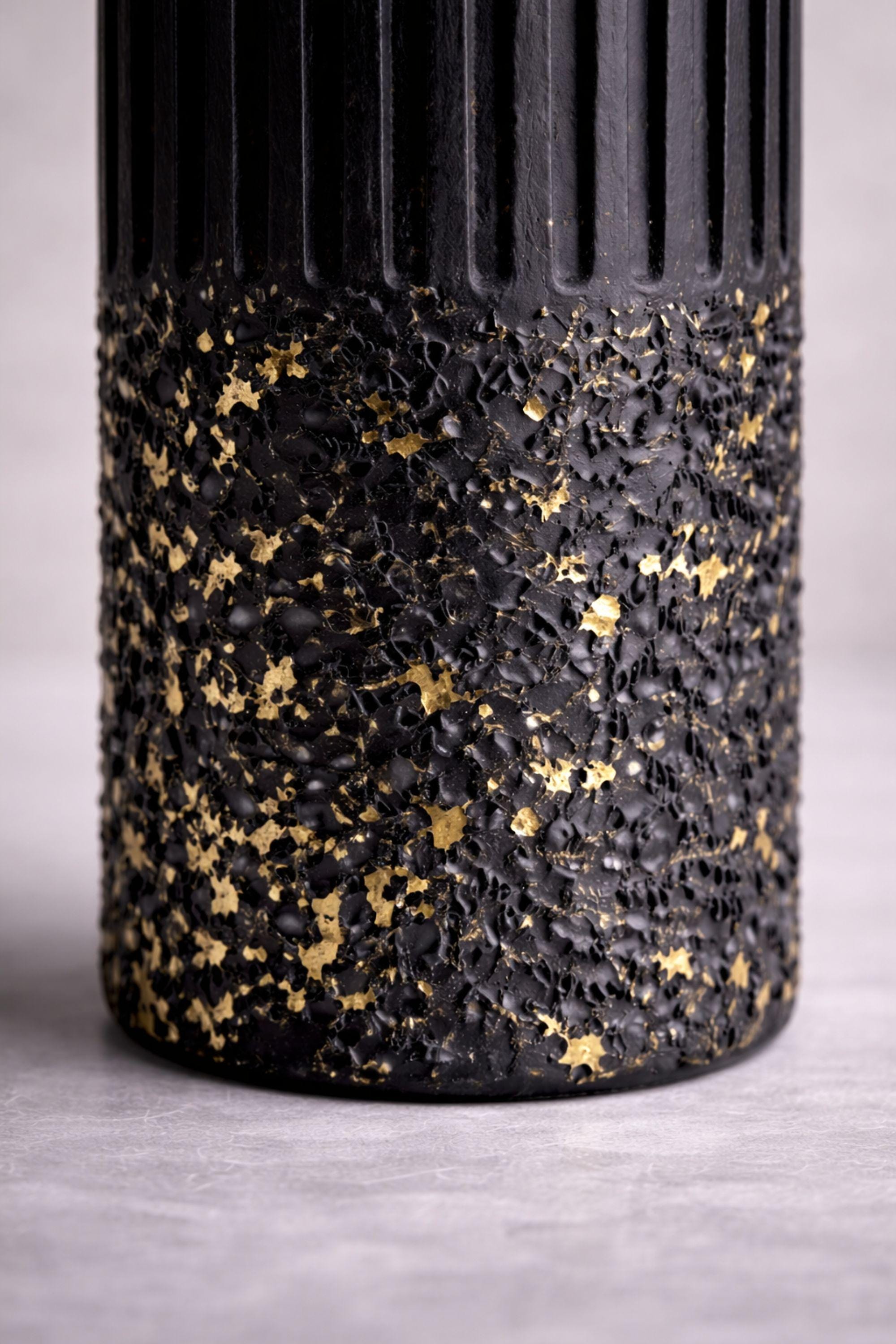 Macro close-up of textured black wax surface with scattered gold flecks. Fine details reveal handcrafted texture, layered wax application, and natural material variation, emphasizing the artisanal quality of this sculptural object.