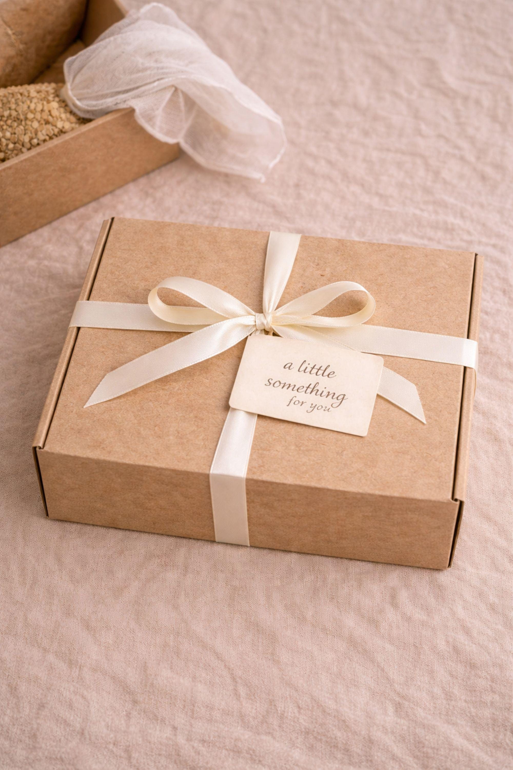 Miscarriage gift box featuring a soft cream knit blanket with lace ribbon, sage teddy bear in white ceramic mug with gold spoon, handmade soap bar, crocheted flower, and wrapped towel arranged in kraft box on neutral beige background with overlay “Holding you in This Loss.” Pregnancy loss care package designed as baby loss sympathy gift and comfort support for grieving mothers.