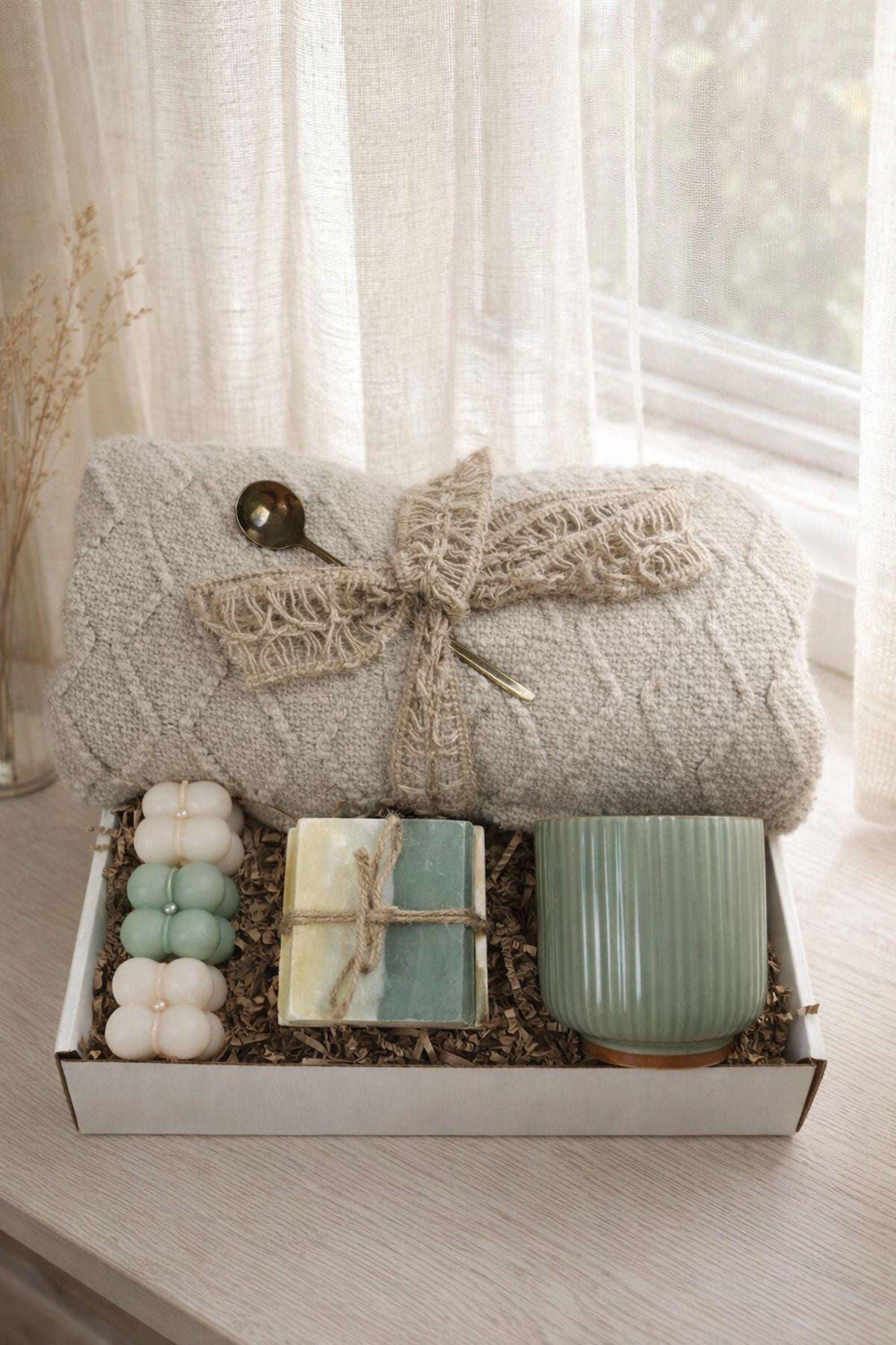 Sending You Hugs grief support gift box with sage knit blanket, ribbed green ceramic mug, handmade two-tone artisan soap, stainless steel spoon, and three bubble candles arranged inside kraft box on warm beige linen background. Sympathy care package designed for comfort during difficult times, loss support, thinking of you gift, and emotional encouragement.