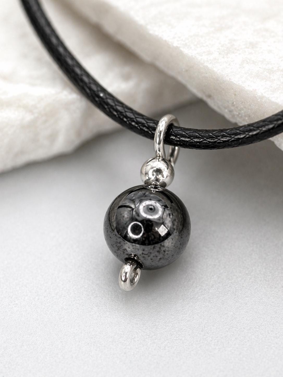 Macro close-up of hematite necklace with polished round gemstone pendant, black adjustable cord choker, minimalist protection jewelry showing natural stone shine and silver details