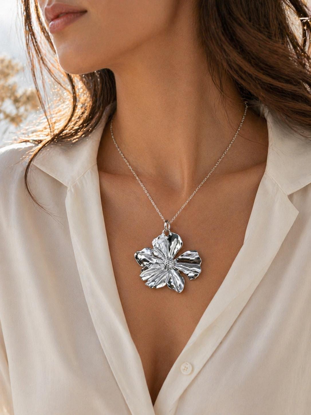 Woman wearing silver flower necklace with large floral pendant, elegant statement jewelry on beige blouse, romantic feminine necklace for everyday wear and special occasions