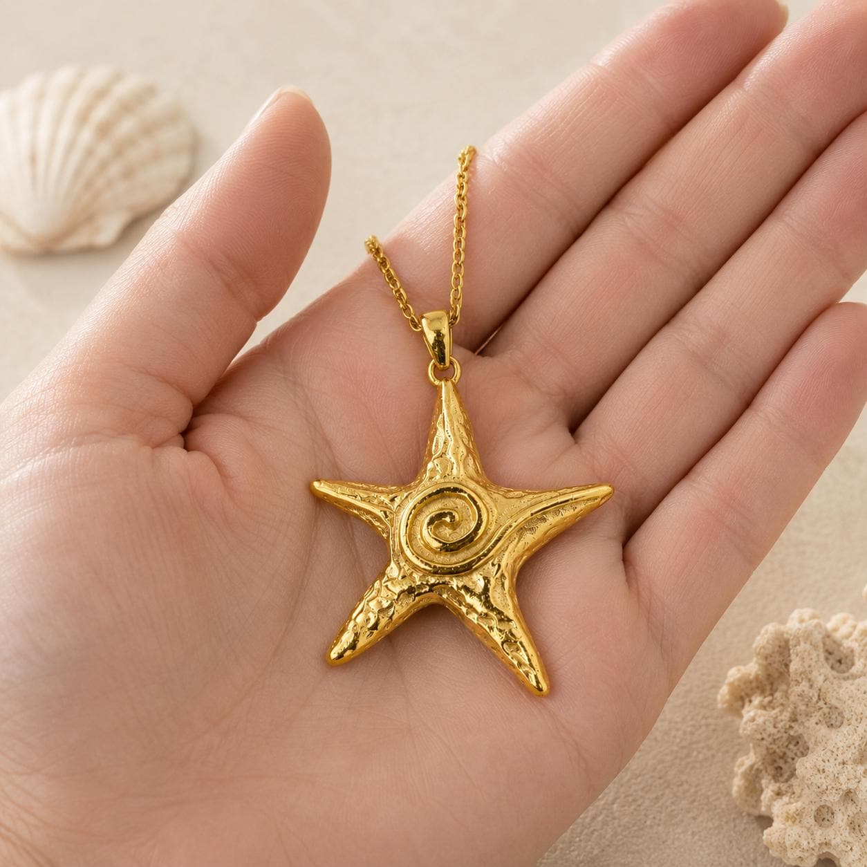 Gold star necklace with textured starfish pendant and spiral center detail resting on an open hand, highlighting the statement size, polished gold finish, and ocean-inspired coastal design.