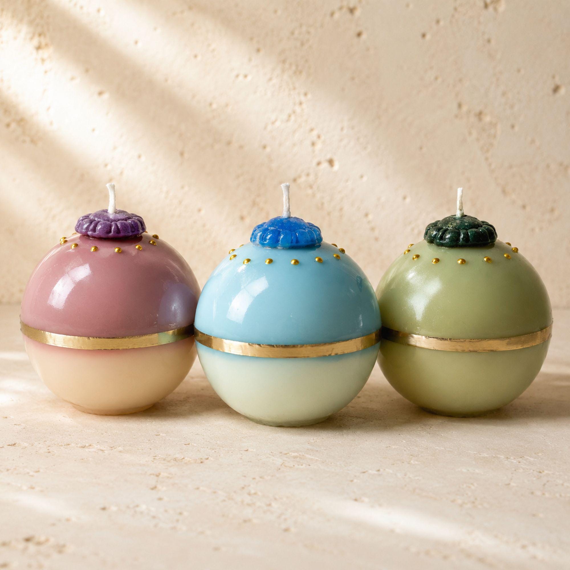 Gilded Orb Collection handmade decorative sphere candles in three color options: Amethyst Blush pink and purple, Azure Mist aqua blue, and Emerald Mist pale green with dark green accents. Unique gold accent ball candles designed as colorful sculptural home decor and elegant handmade gifts.