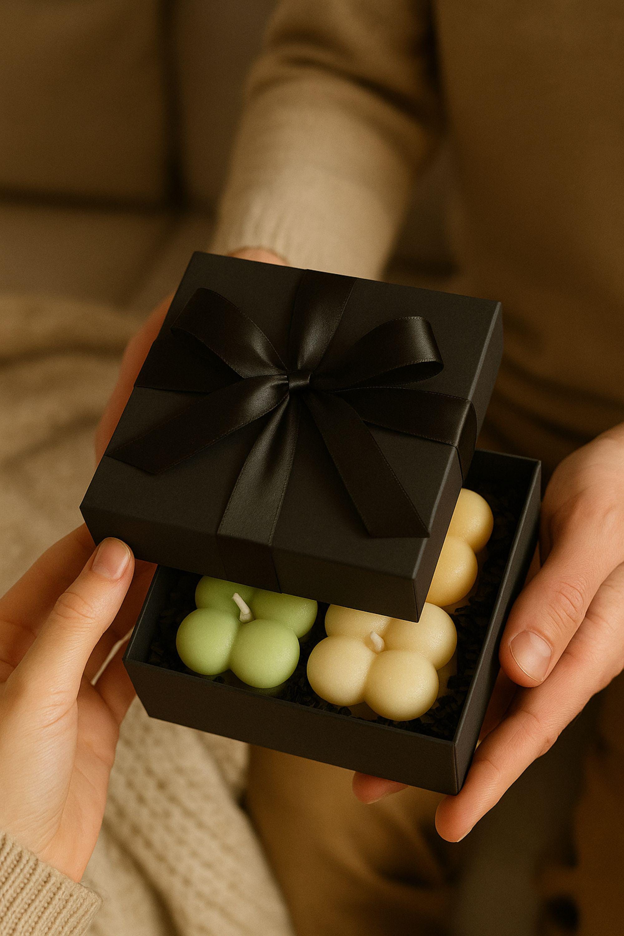 Elegant black gift box with satin bow and bubble candles inside, photographed in a festive Christmas setting. Small luxury candle gift for women.