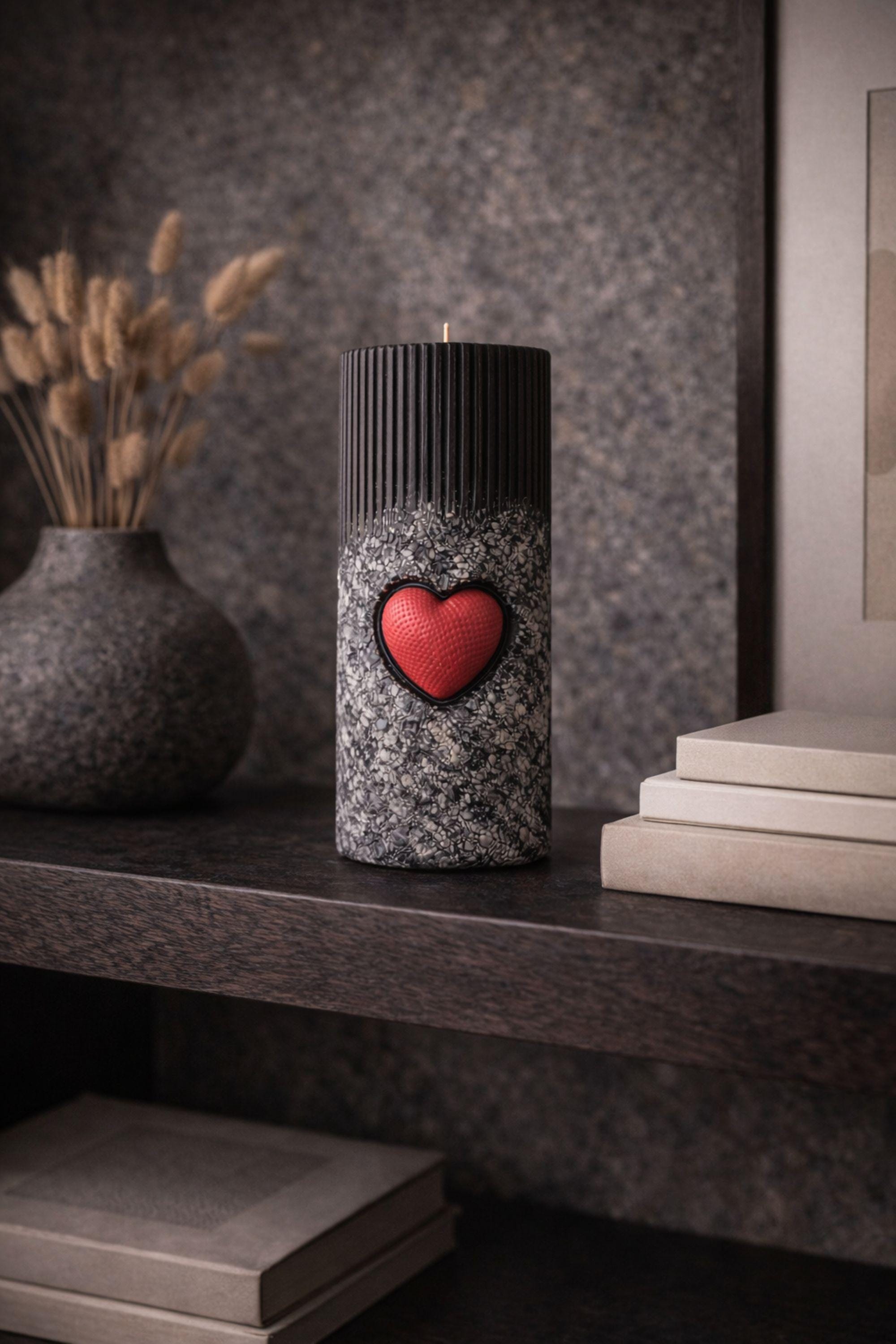 Statement object candle displayed as a modern sculptural decor piece on a stone surface. Handmade black pillar candle with black, gray and white stone-like texture and heart detail. Designer candle object for contemporary home decor, minimalist interiors, shelves and side tables.
