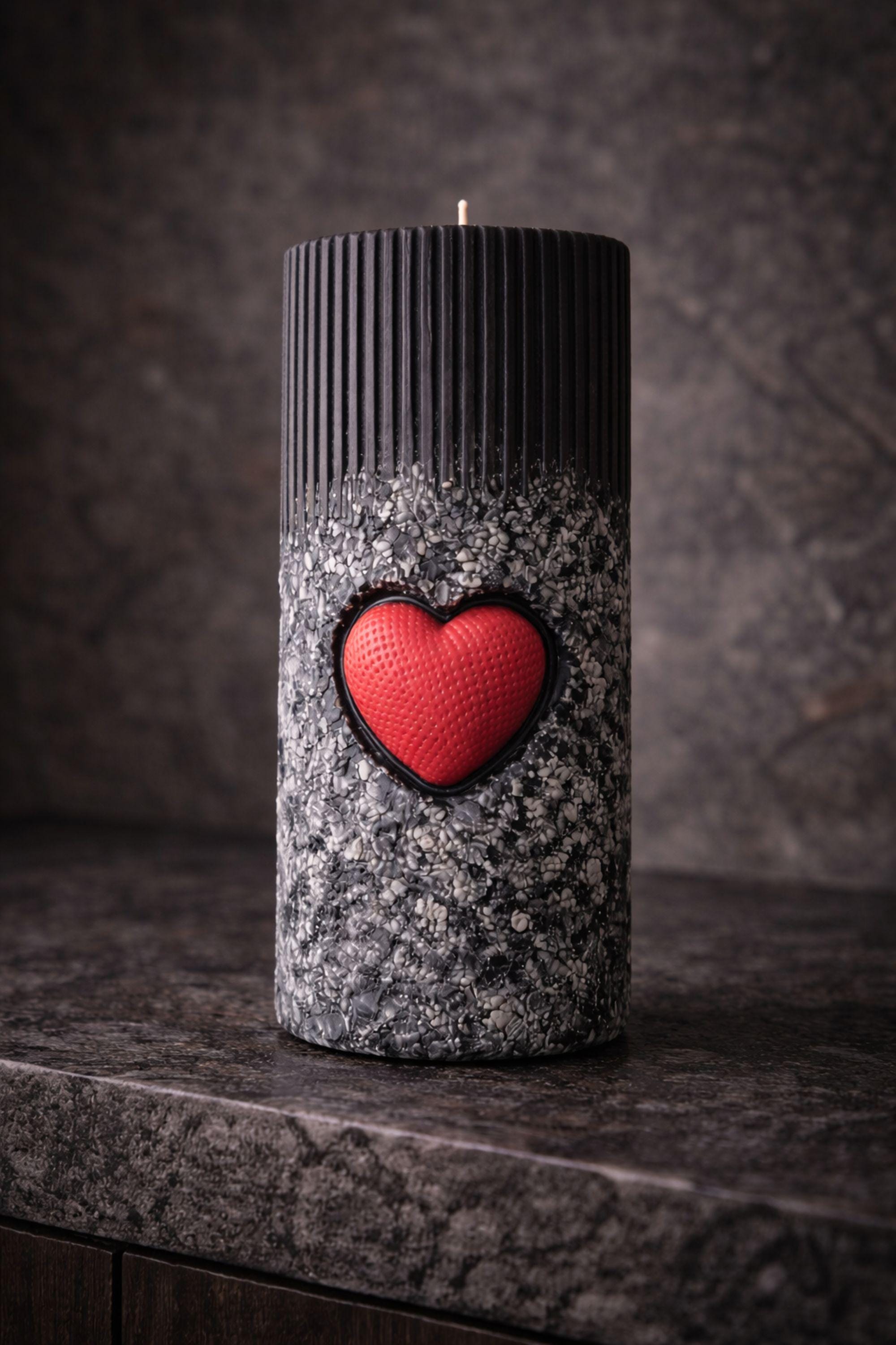 Statement object candle displayed as a modern sculptural decor piece on a stone surface. Handmade black pillar candle with black, gray and white stone-like texture and heart detail. Designer candle object for contemporary home decor, minimalist interiors, shelves and side tables.