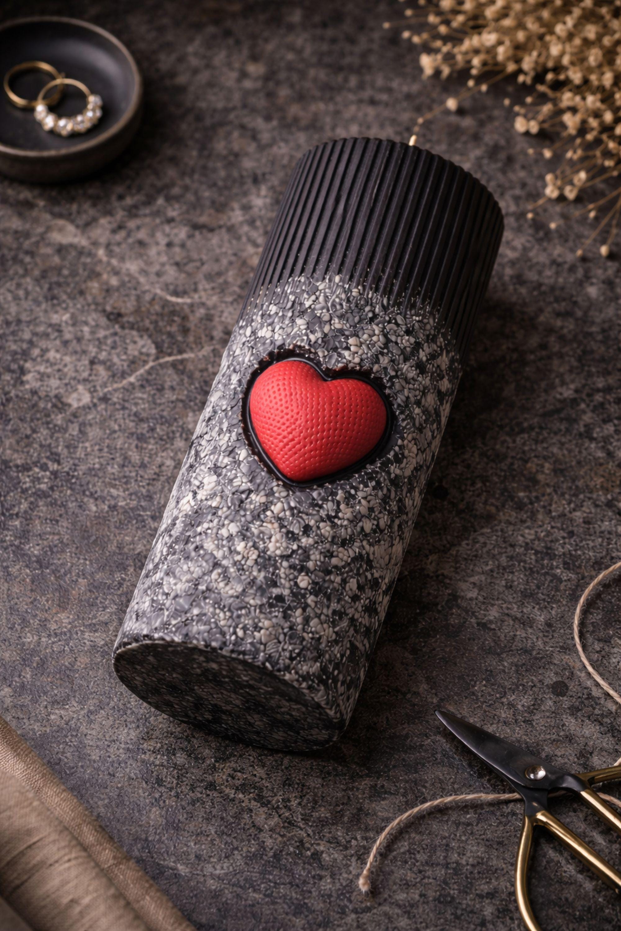 Statement object candle displayed as a modern sculptural decor piece on a stone surface. Handmade black pillar candle with black, gray and white stone-like texture and heart detail. Designer candle object for contemporary home decor, minimalist interiors, shelves and side tables.