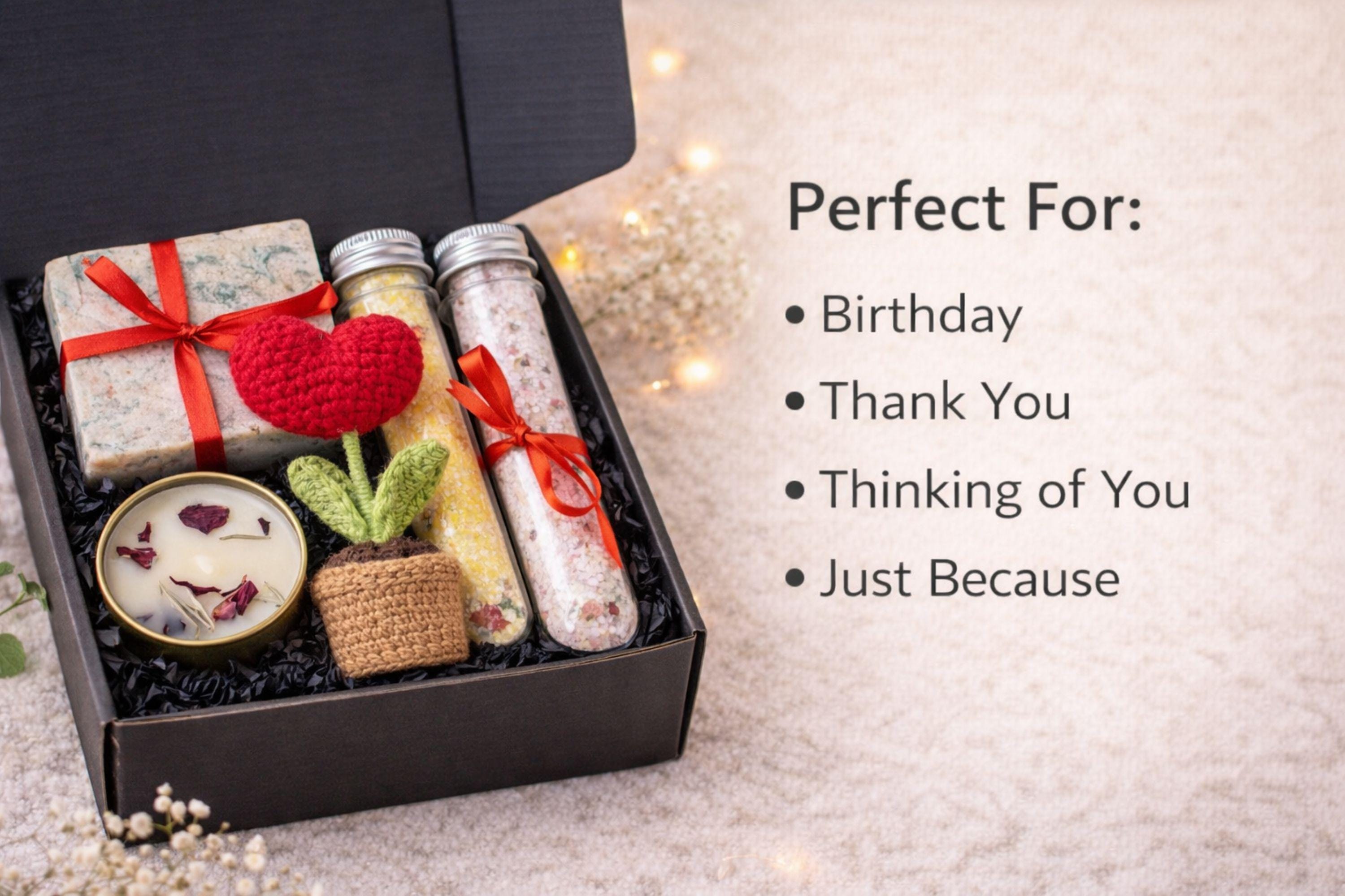 Handmade crochet flower gift box with crochet flower in a pot, handmade soap, botanical candle in a tin, and two bath salt tubes arranged in a black gift box. Thoughtful comfort gift designed to show care and appreciation. Perfect thinking of you gift, friendship gift, or unique handmade present for her, beautifully packaged and ready to give.
