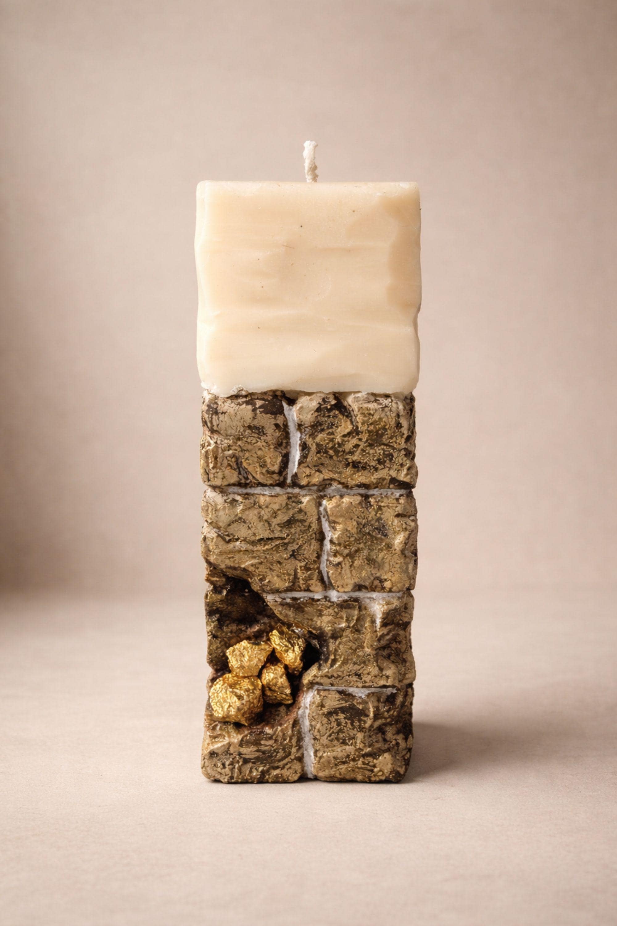 Sculptural ritual candle handmade from wax with textured stone-inspired surface and metallic gold detailing, designed as a modern altar decor object. Minimalist sculptural candle that can be displayed as art or burned intentionally. Artisan wax sculpture candle for ritual space, meditation altar, or modern interior decor. Unique handcrafted statement candle with raw texture and architectural form, photographed on neutral background.