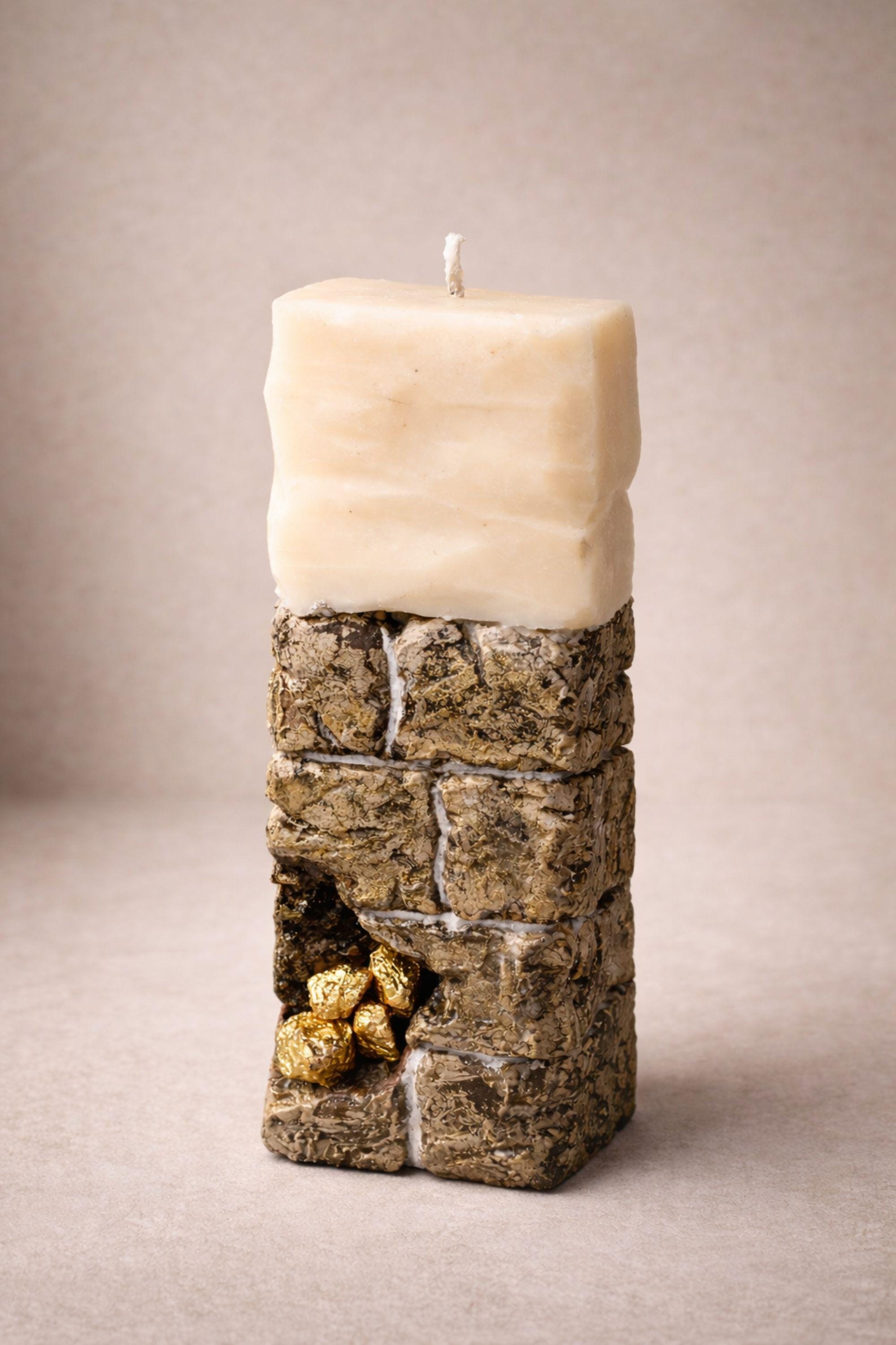 Sculptural ritual candle handmade from wax with textured stone-inspired surface and metallic gold detailing, designed as a modern altar decor object. Minimalist sculptural candle that can be displayed as art or burned intentionally. Artisan wax sculpture candle for ritual space, meditation altar, or modern interior decor. Unique handcrafted statement candle with raw texture and architectural form, photographed on neutral background.