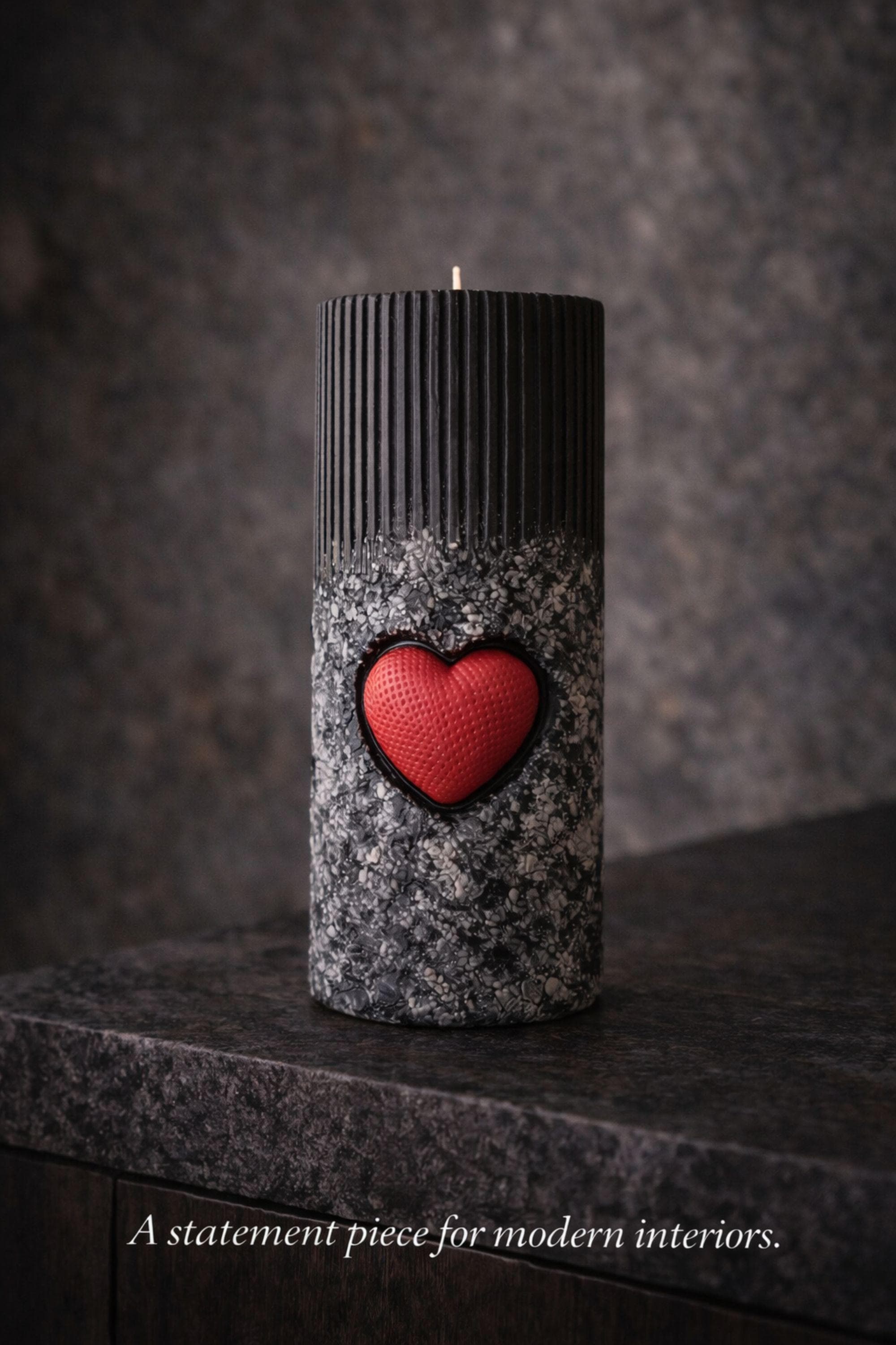 Statement object candle displayed as a modern sculptural decor piece on a stone surface. Handmade black pillar candle with black, gray and white stone-like texture and heart detail. Designer candle object for contemporary home decor, minimalist interiors, shelves and side tables.