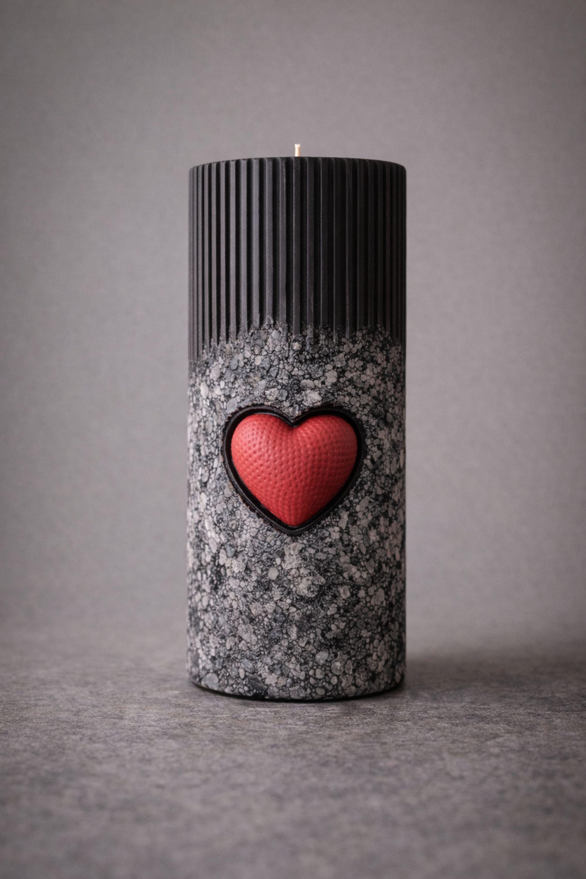 Statement object candle displayed as a modern sculptural decor piece on a stone surface. Handmade black pillar candle with black, gray and white stone-like texture and heart detail. Designer candle object for contemporary home decor, minimalist interiors, shelves and side tables.