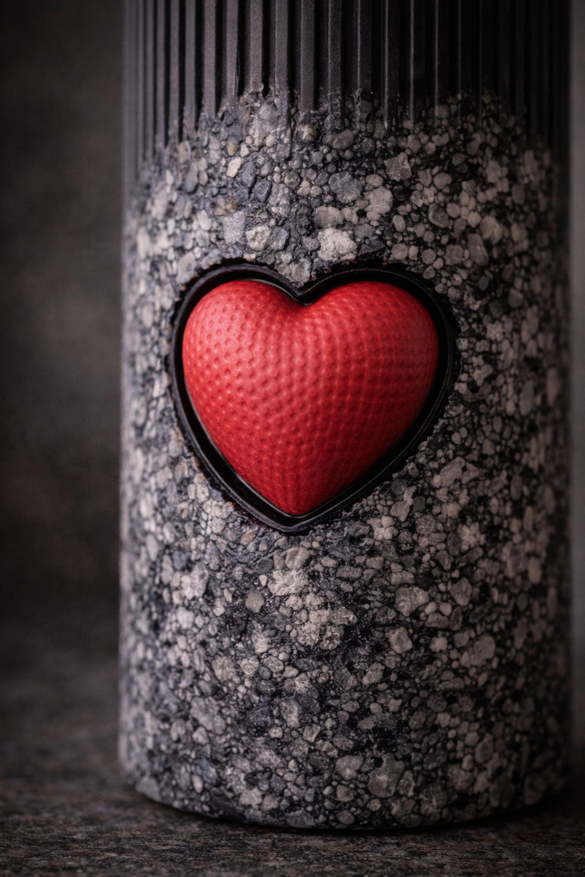 Statement object candle displayed as a modern sculptural decor piece on a stone surface. Handmade black pillar candle with black, gray and white stone-like texture and heart detail. Designer candle object for contemporary home decor, minimalist interiors, shelves and side tables.