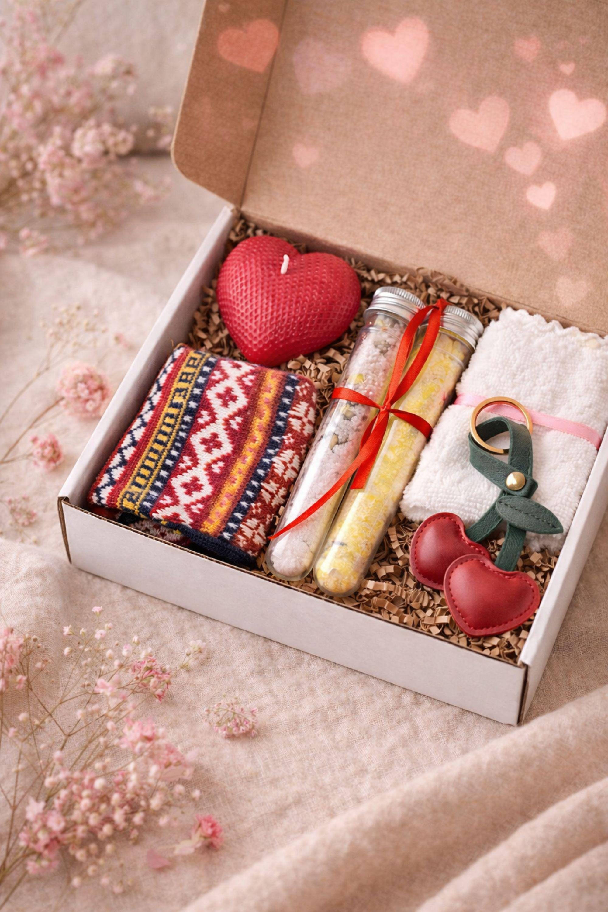 Thinking of you gift box with handmade heart candle, cozy knitted socks, bath salt tubes tied with red ribbon, soft cotton washcloth, and leather heart keychain arranged inside a kraft gift box. Small meaningful comfort gift designed as a care package for her, perfect for sending love, warmth, and support during long distance moments, stressful times, or just because. Handmade cozy gift set ready to give.