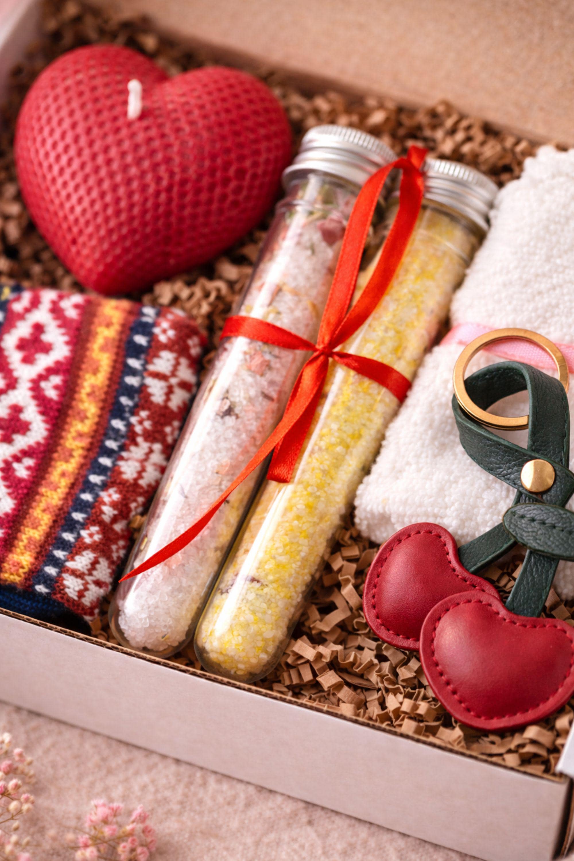 Close-up of Valentine gift details including a red heart shaped candle, leather heart keychain, bath salt tubes, and soft washcloth arranged in a cozy handmade care package. Romantic Valentine gift for her focused on warmth, love, and emotional connection, ideal for long distance Valentine gifts, thoughtful romantic gestures, and heartfelt handmade presents.