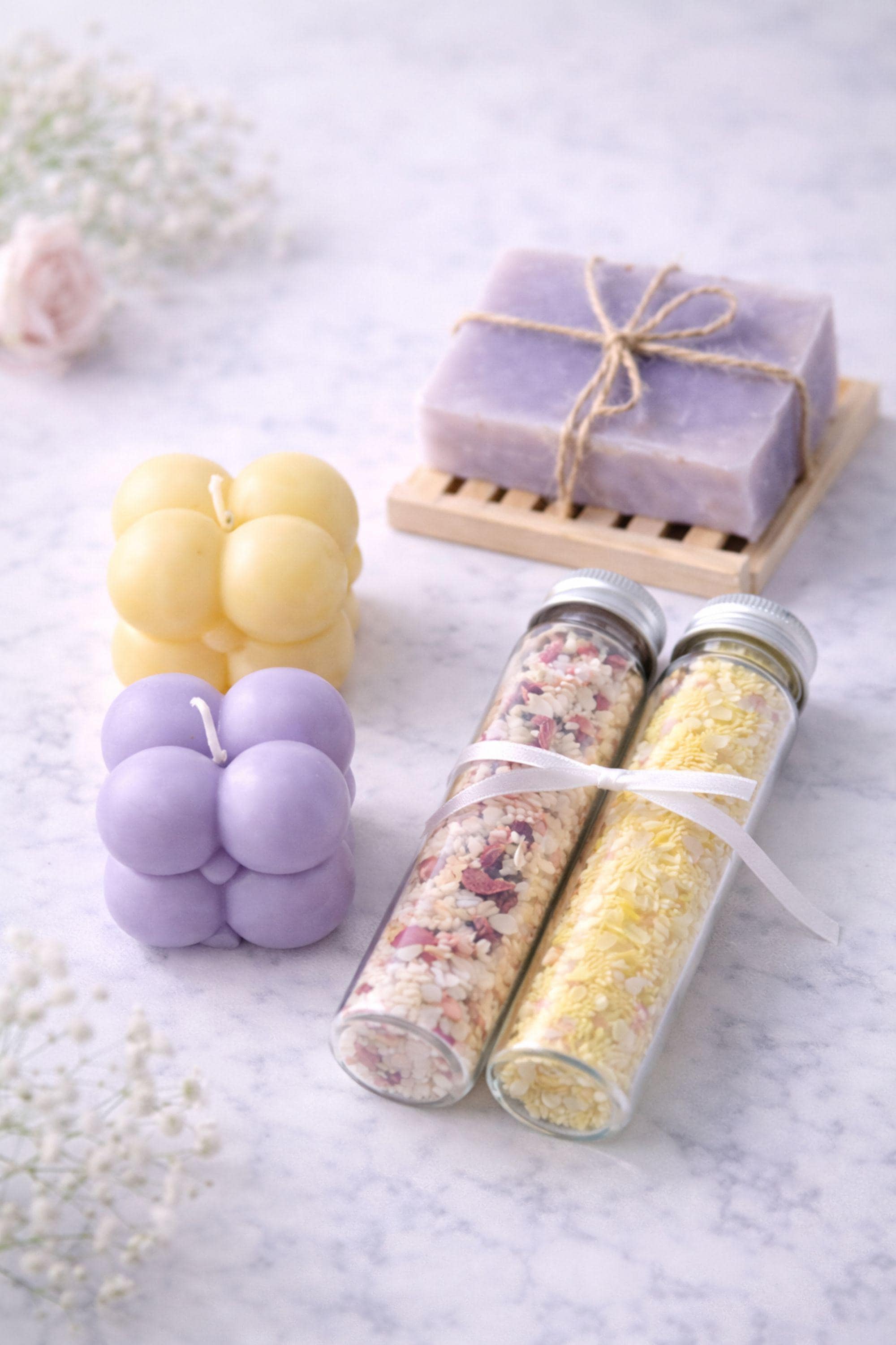 Flat lay image showing everything included in a gift for her box: handmade bubble candles, natural soap on a wooden soap dish, and two glass tubes filled with bath salts. Items are neatly arranged on a clean background to clearly display contents of a compact 6x6 inch handmade gift box.