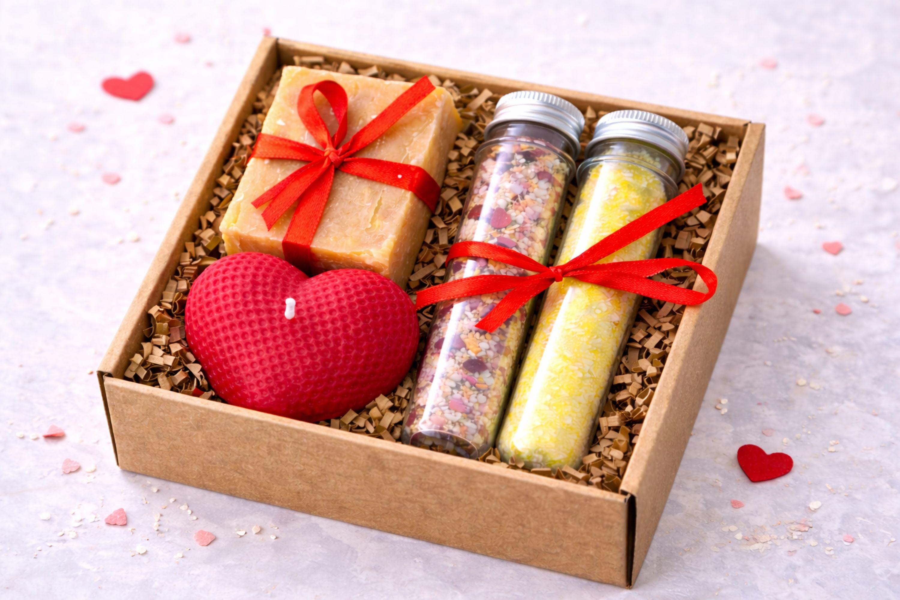 Romantic handmade gift box for her displayed open in a kraft box with a red heart candle, natural soap tied with a red ribbon, and two glass tubes filled with bath salts. This thoughtful love gift features warm red accents and handcrafted details, presented on a clean neutral background. A romantic gift set designed to express love in a simple, elegant way, perfect as a romantic gift for her, anniversary present, or heartfelt love surprise.
