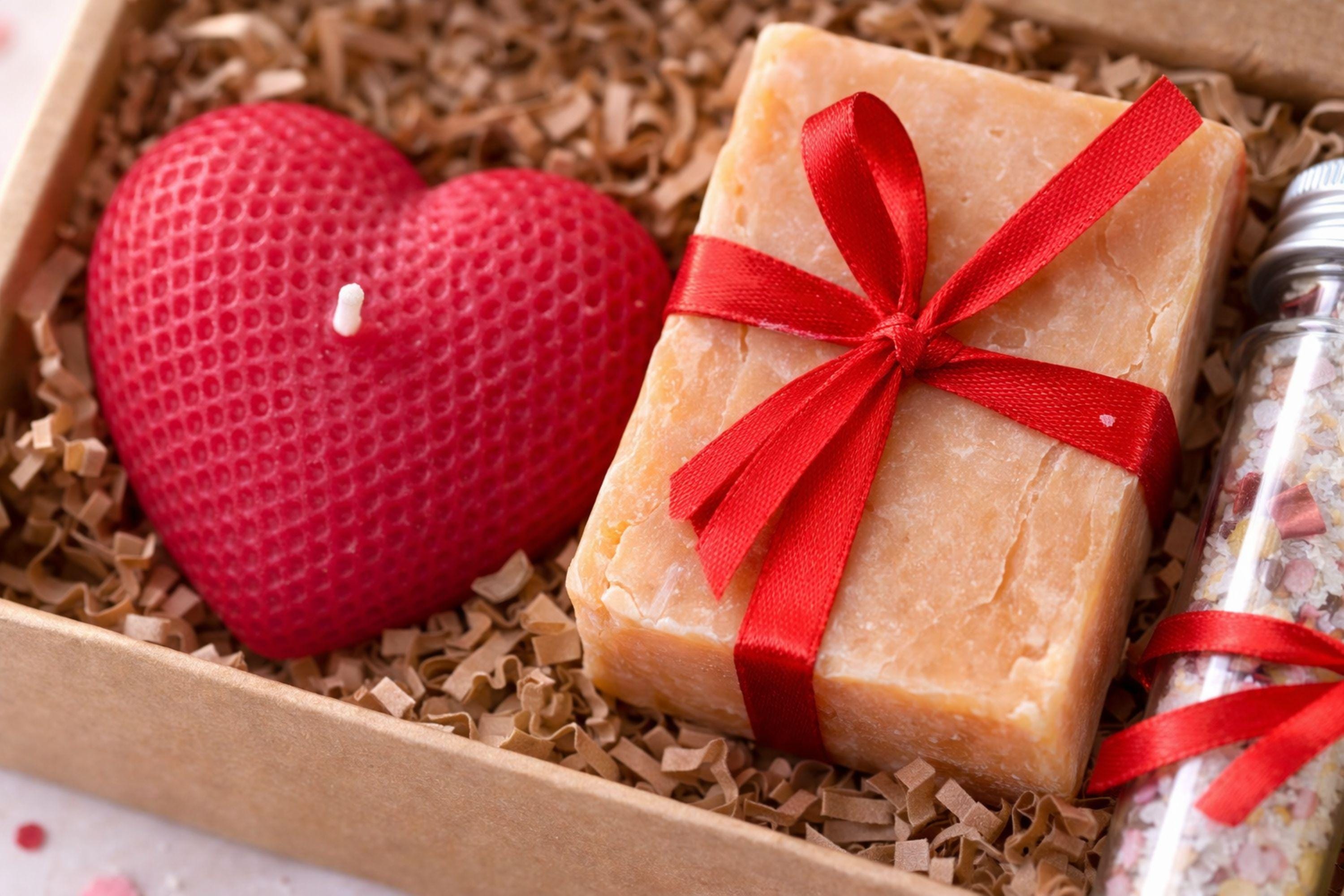 Romantic handmade gift box for her displayed open in a kraft box with a red heart candle, natural soap tied with a red ribbon, and two glass tubes filled with bath salts. This thoughtful love gift features warm red accents and handcrafted details, presented on a clean neutral background. A romantic gift set designed to express love in a simple, elegant way, perfect as a romantic gift for her, anniversary present, or heartfelt love surprise.