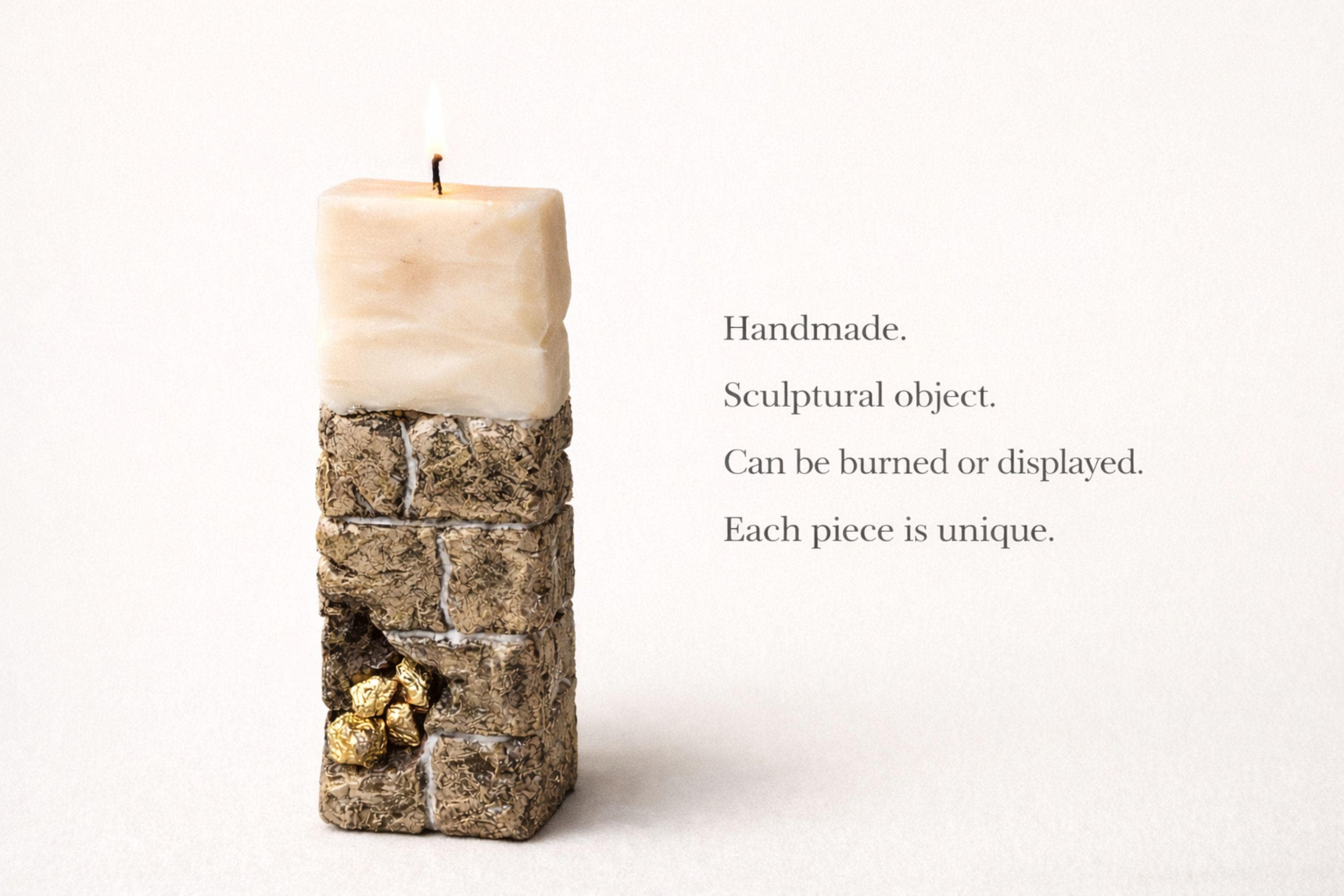 Sculptural ritual candle handmade from wax with textured stone-inspired surface and metallic gold detailing, designed as a modern altar decor object. Minimalist sculptural candle that can be displayed as art or burned intentionally. Artisan wax sculpture candle for ritual space, meditation altar, or modern interior decor. Unique handcrafted statement candle with raw texture and architectural form, photographed on neutral background.