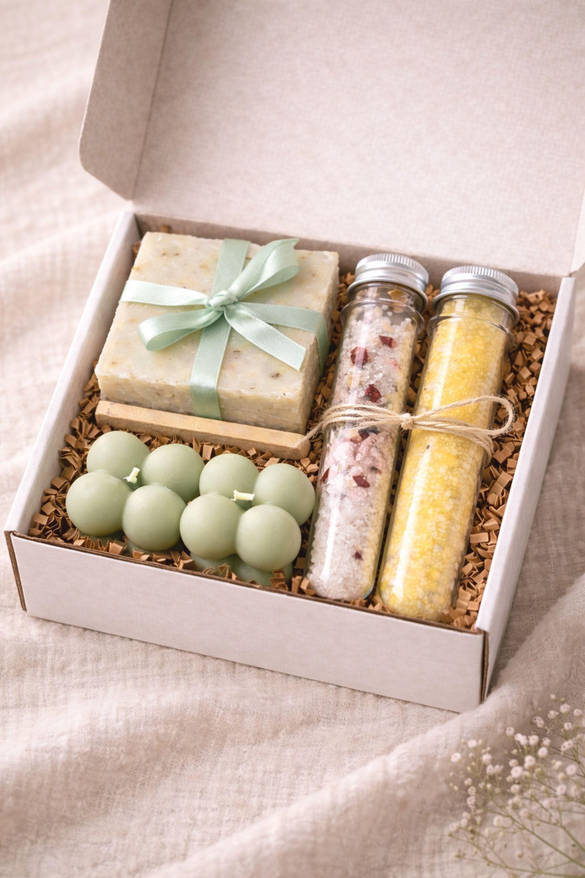 Minimalist cozy gift box displayed open on a neutral linen surface, featuring handmade sage bubble candles, natural soap tied with a soft ribbon, and two glass tubes of bath salts arranged neatly inside a white box. Calm home gift set designed for everyday self care, slow living routines, and cozy home moments, ideal as a minimalist handmade candle and soap set for a peaceful interior atmosphere.