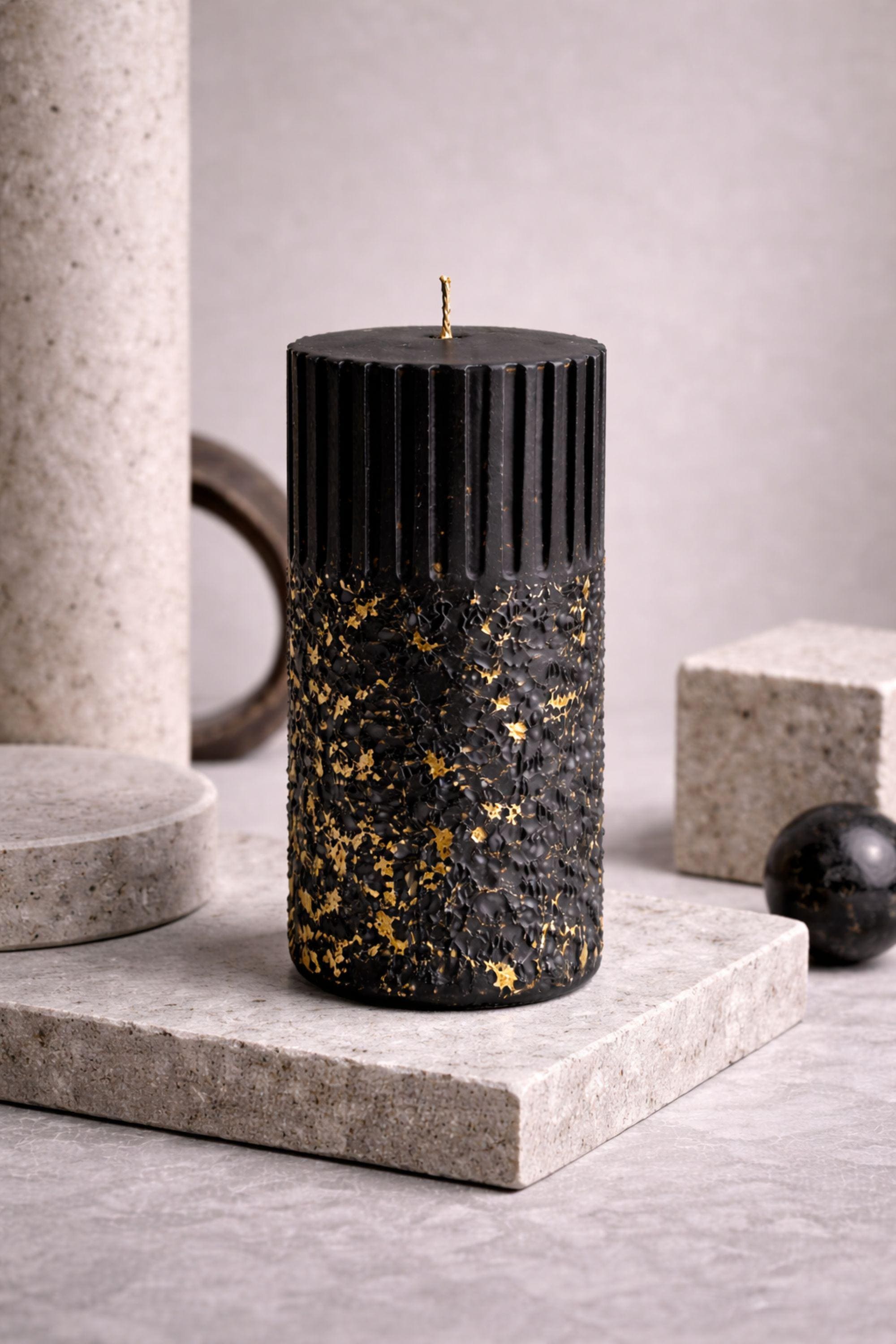 Minimal photograph of a single black sculptural wax object on a neutral background with ample negative space. The clean vertical form and restrained gold flecks reinforce its identity as a modern AuraBox design object.