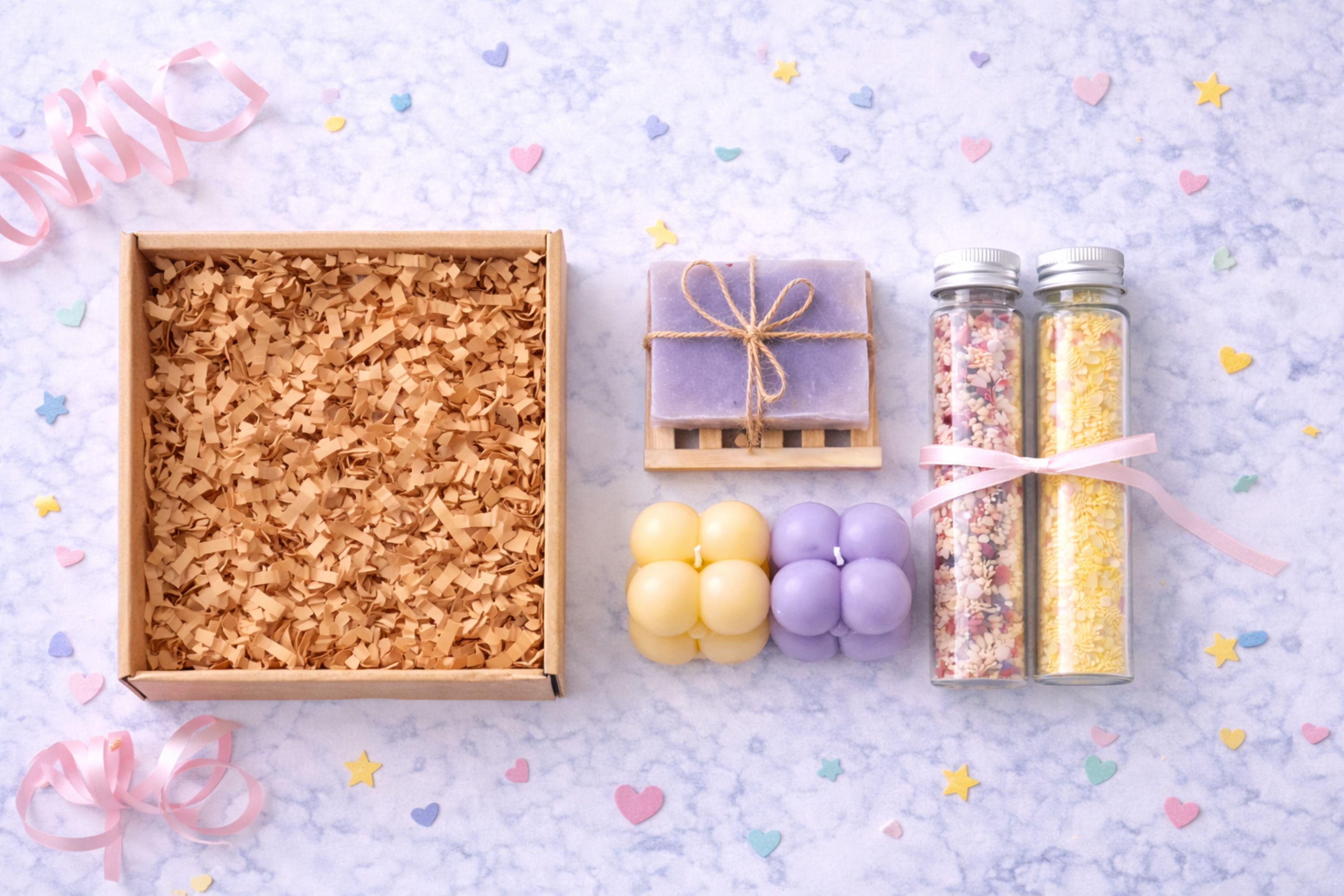 Flat lay photograph showing everything included in a gift for best friend box: handmade bubble candles, natural soap on a wooden dish, and two glass tubes filled with bath salts. Items are neatly arranged on a light background to clearly show contents of a small 6x6 inch handmade gift box designed for fun and cozy gifting.