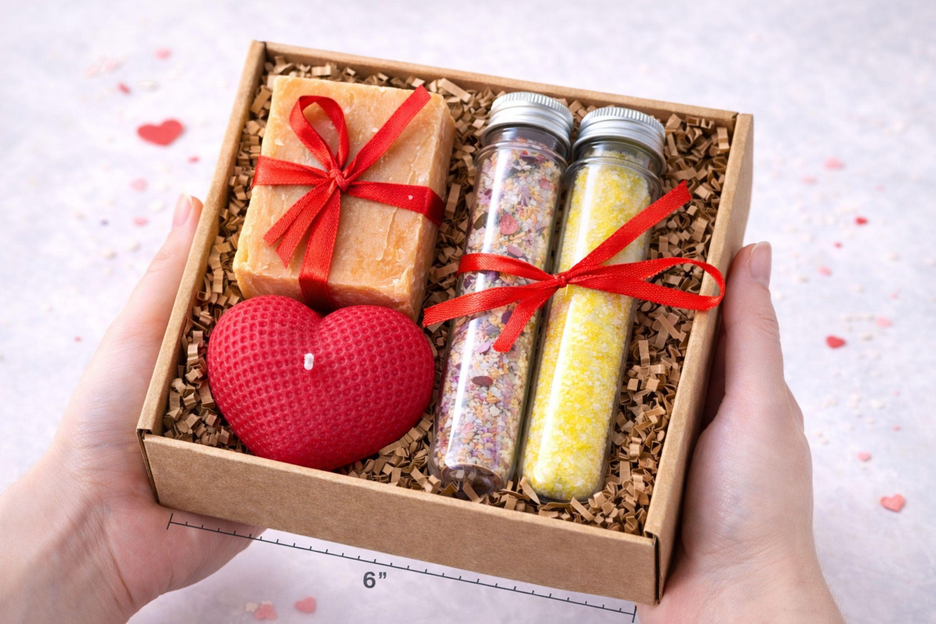 Romantic handmade gift box for her displayed open in a kraft box with a red heart candle, natural soap tied with a red ribbon, and two glass tubes filled with bath salts. This thoughtful love gift features warm red accents and handcrafted details, presented on a clean neutral background. A romantic gift set designed to express love in a simple, elegant way, perfect as a romantic gift for her, anniversary present, or heartfelt love surprise.