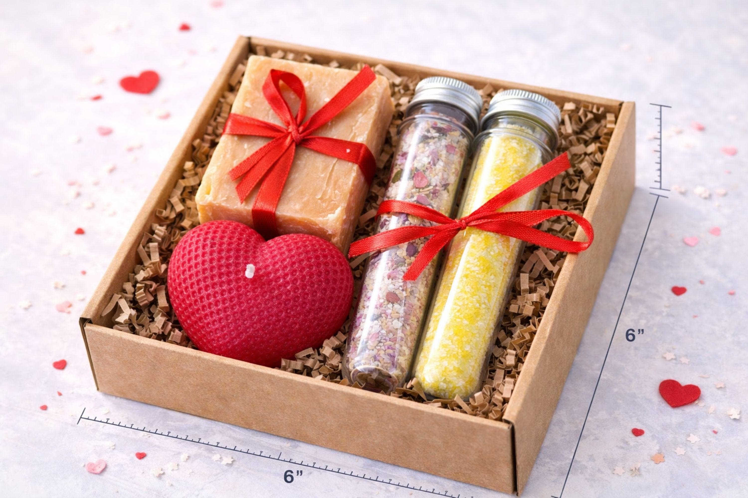 Romantic handmade gift box for her displayed open in a kraft box with a red heart candle, natural soap tied with a red ribbon, and two glass tubes filled with bath salts. This thoughtful love gift features warm red accents and handcrafted details, presented on a clean neutral background. A romantic gift set designed to express love in a simple, elegant way, perfect as a romantic gift for her, anniversary present, or heartfelt love surprise.