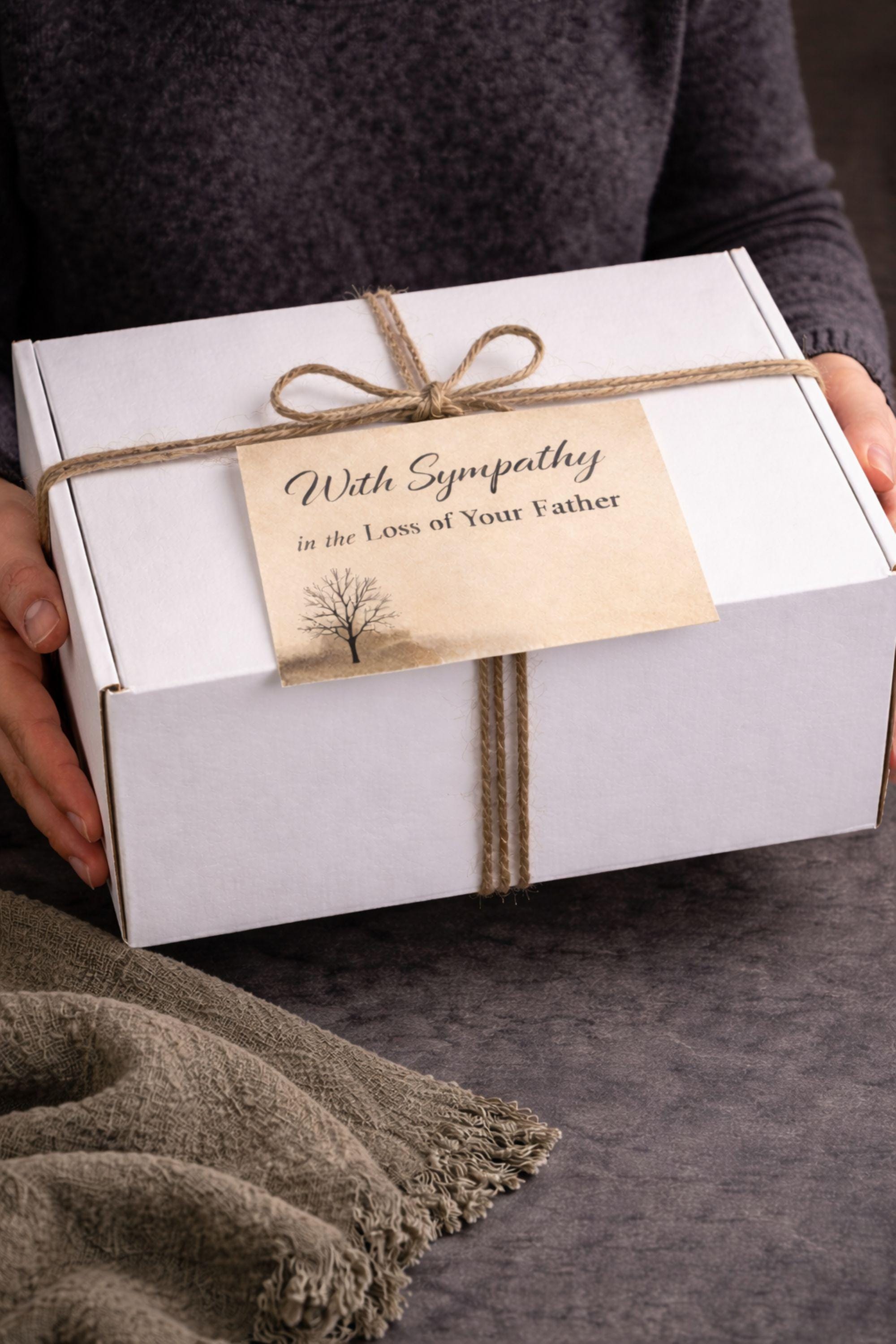 Loss of father sympathy gift box displayed on dark charcoal background with cozy olive knit blanket, handmade pillar candle with textured stone-style base and subtle gold accents, natural handmade soap on wooden holder, ceramic mug with spoon, thoughtful bereavement care package designed for condolence support, memorial gift for grieving family after dad loss, meaningful comfort present during funeral or remembrance