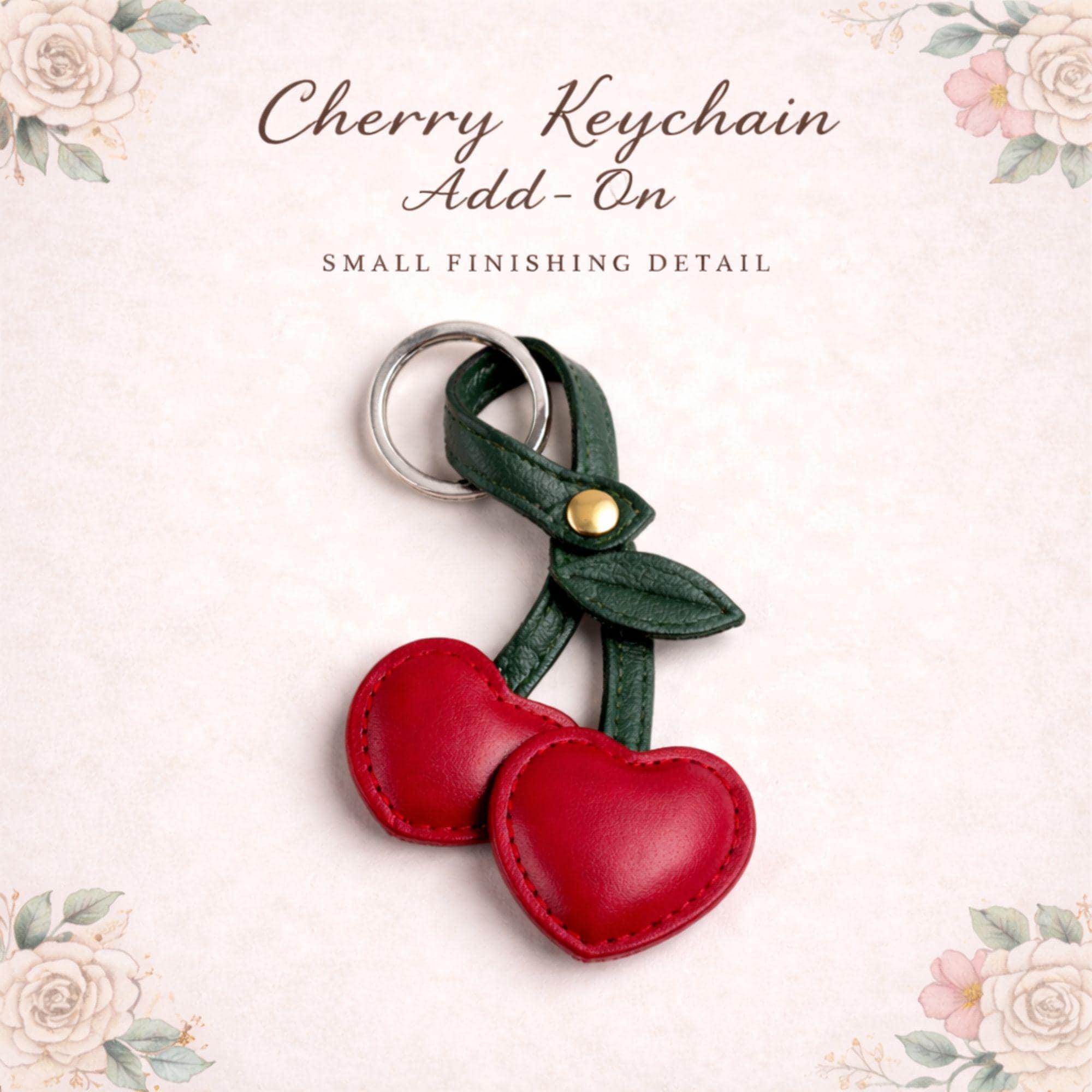 Close up of cherry keychain add on showing stitched faux leather texture, red heart shaped cherries, green stem, and silver key ring hardware. Detailed view highlights craftsmanship and quality of this cute bag charm gift box upgrade accessory.
