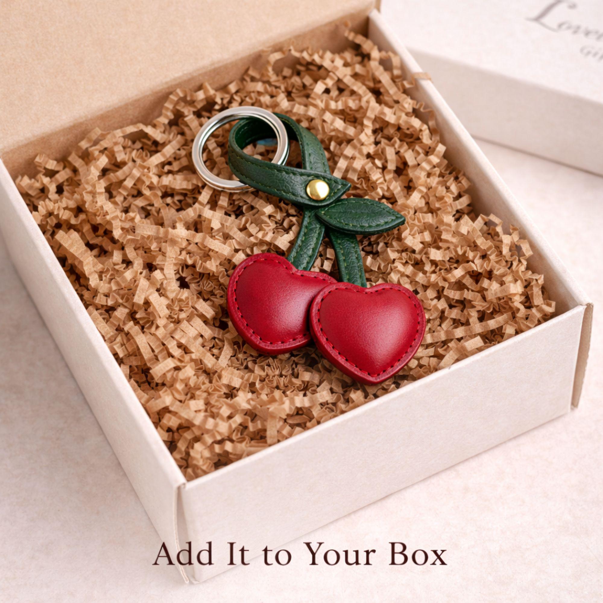 Red cherry keychain add on displayed on neutral floral background. Faux leather bag charm with green stem and silver ring styled as gift box upgrade. Cute aesthetic accessory for build your own gift box, birthday gift, Valentine care package, or cozy self care set.