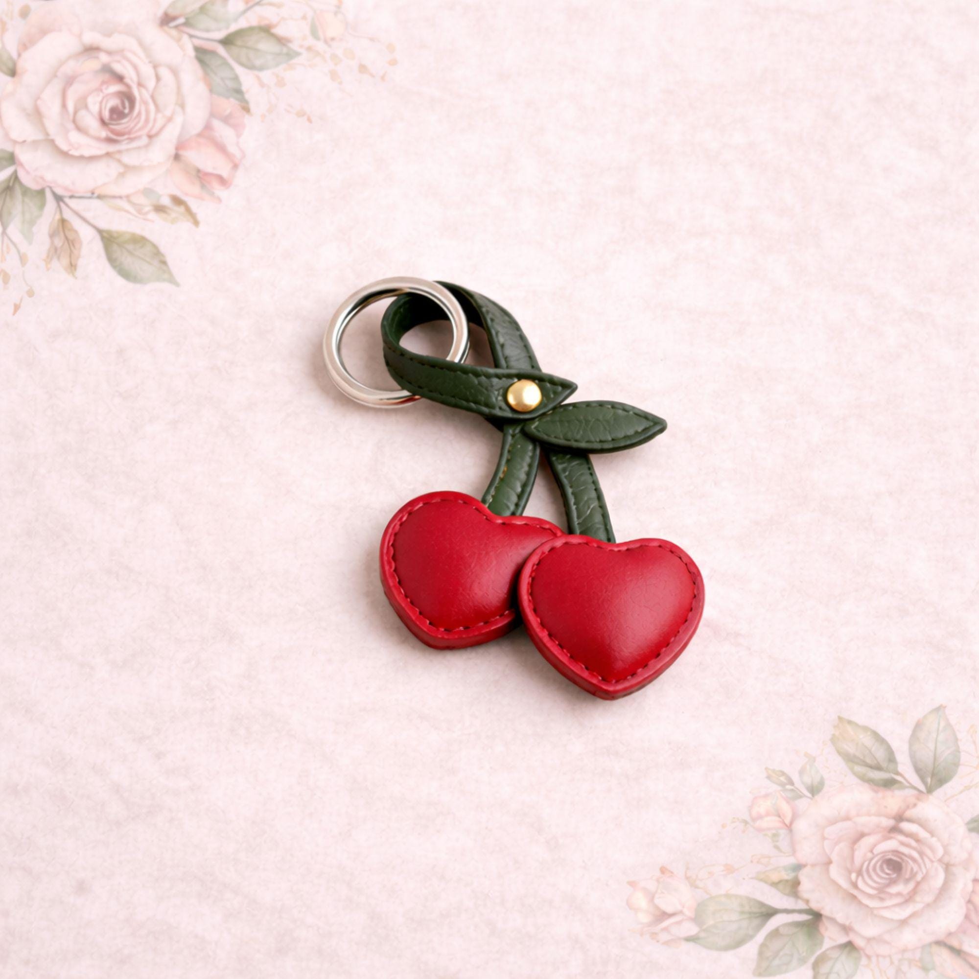Red cherry keychain add on displayed on neutral floral background. Faux leather bag charm with green stem and silver ring styled as gift box upgrade. Cute aesthetic accessory for build your own gift box, birthday gift, Valentine care package, or cozy self care set.