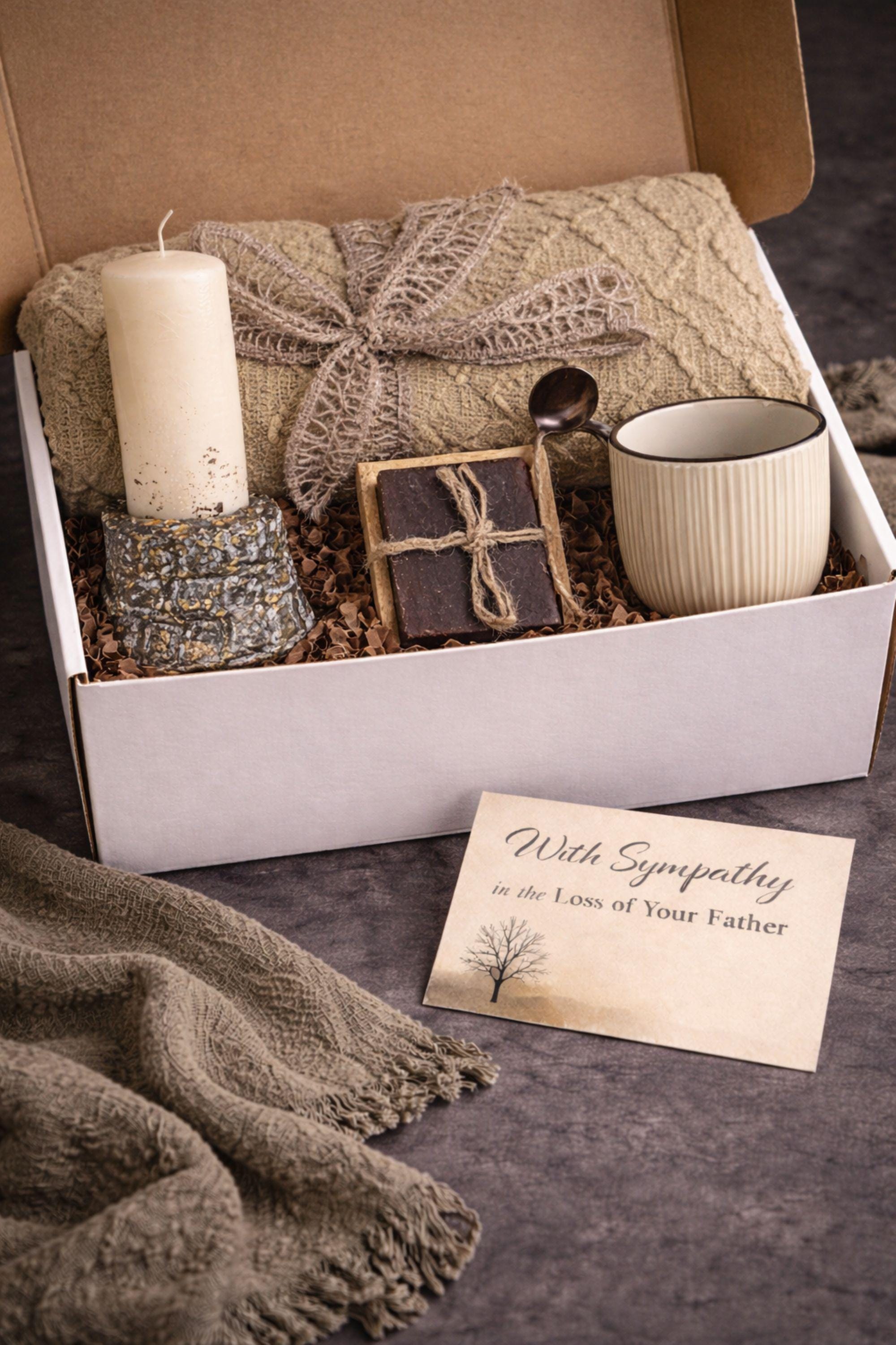 Loss of father sympathy gift box displayed on dark charcoal background with cozy olive knit blanket, handmade pillar candle with textured stone-style base and subtle gold accents, natural handmade soap on wooden holder, ceramic mug with spoon, thoughtful bereavement care package designed for condolence support, memorial gift for grieving family after dad loss, meaningful comfort present during funeral or remembrance