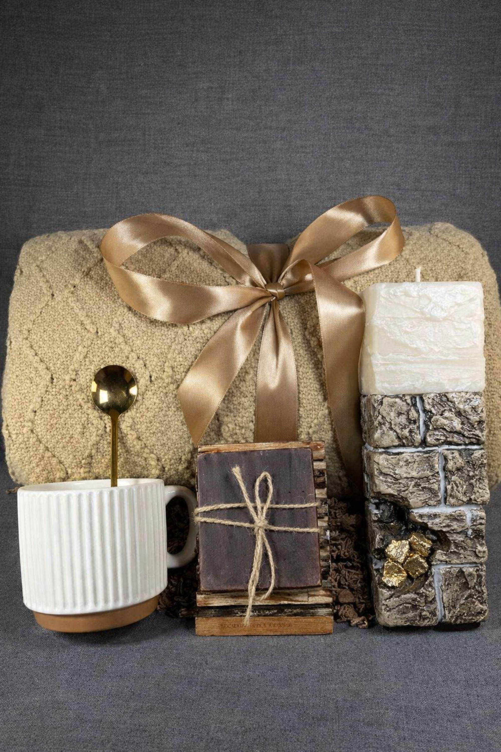 Open white sympathy gift box for loss of wife displayed on neutral mouse grey linen background, featuring soft beige knit blanket tied with satin ribbon, handcrafted 24K textured memorial candle with gold accents, ribbed ceramic mug with spoon, artisan soap on wooden stand, arranged as a thoughtful bereavement care package for grieving husband. Elegant comfort gift for widower, condolence gift box, memorial support present.