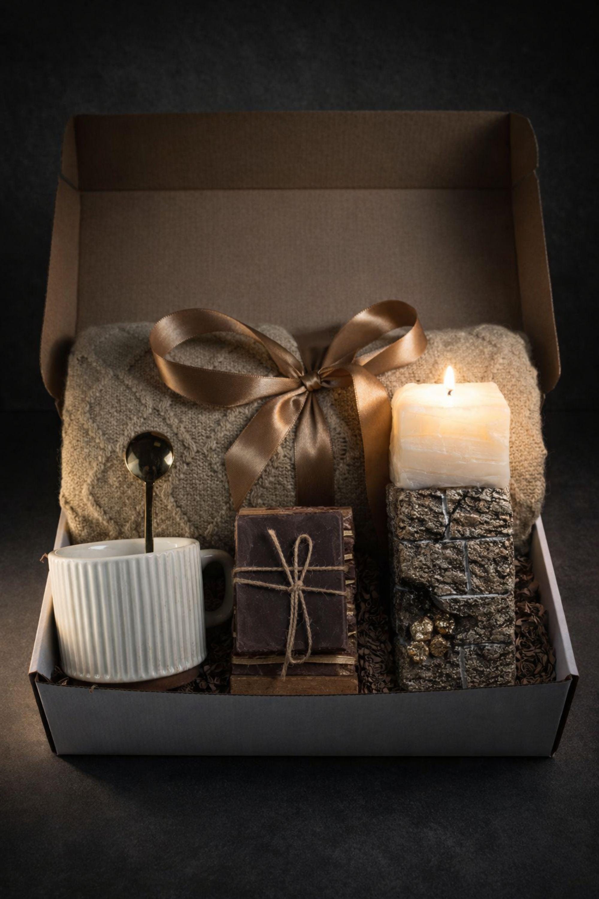 Open white sympathy gift box for loss of wife displayed on neutral mouse grey linen background, featuring soft beige knit blanket tied with satin ribbon, handcrafted 24K textured memorial candle with gold accents, ribbed ceramic mug with spoon, artisan soap on wooden stand, arranged as a thoughtful bereavement care package for grieving husband. Elegant comfort gift for widower, condolence gift box, memorial support present.