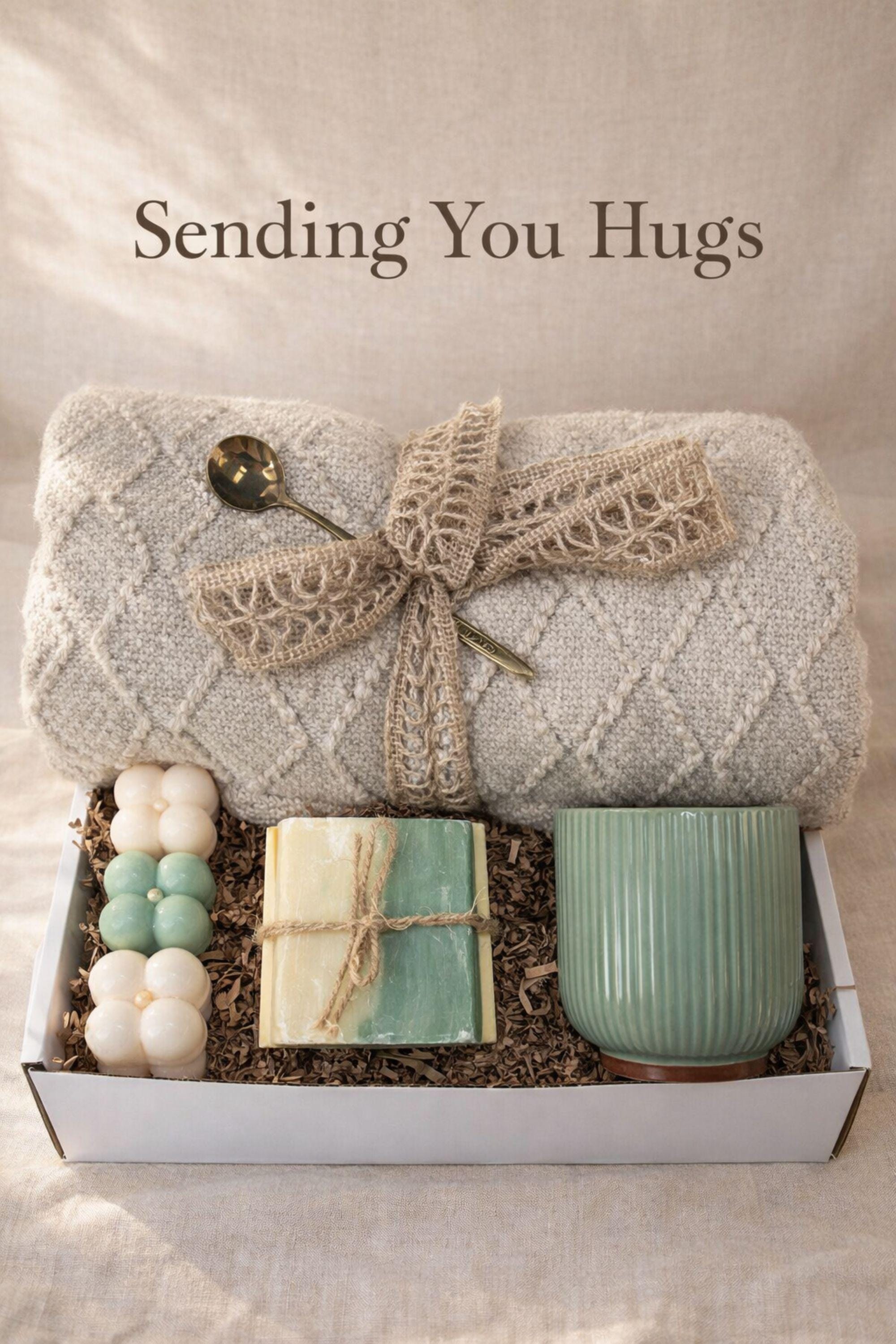 Sending You Hugs grief support gift box with sage knit blanket, ribbed green ceramic mug, handmade two-tone artisan soap, stainless steel spoon, and three bubble candles arranged inside kraft box on warm beige linen background. Sympathy care package designed for comfort during difficult times, loss support, thinking of you gift, and emotional encouragement.